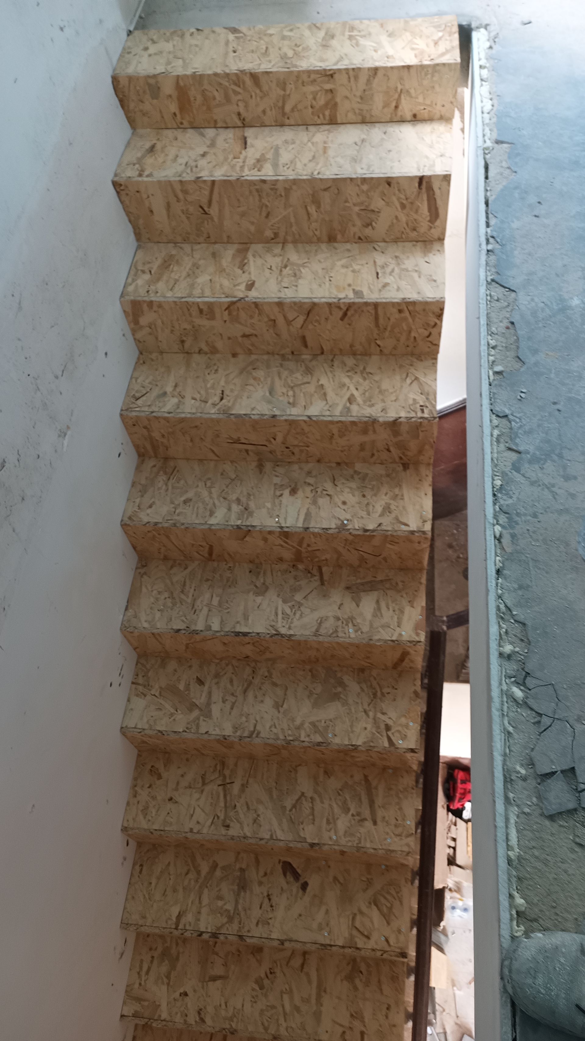 Escada feita de aglomerado, que sobe para uma abertura entre paredes.