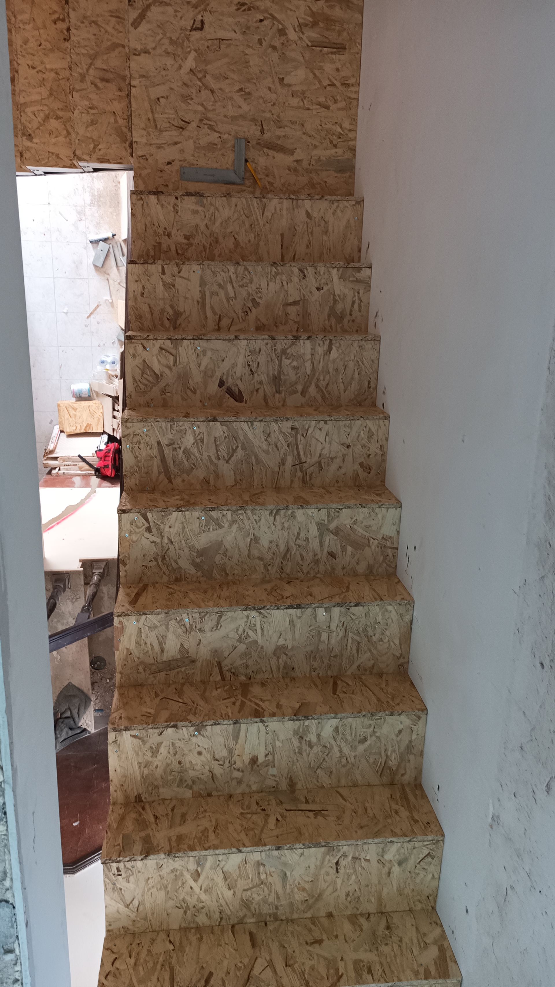 Escada feita de aglomerado, que leva a um andar superior com uma porta visível no topo.