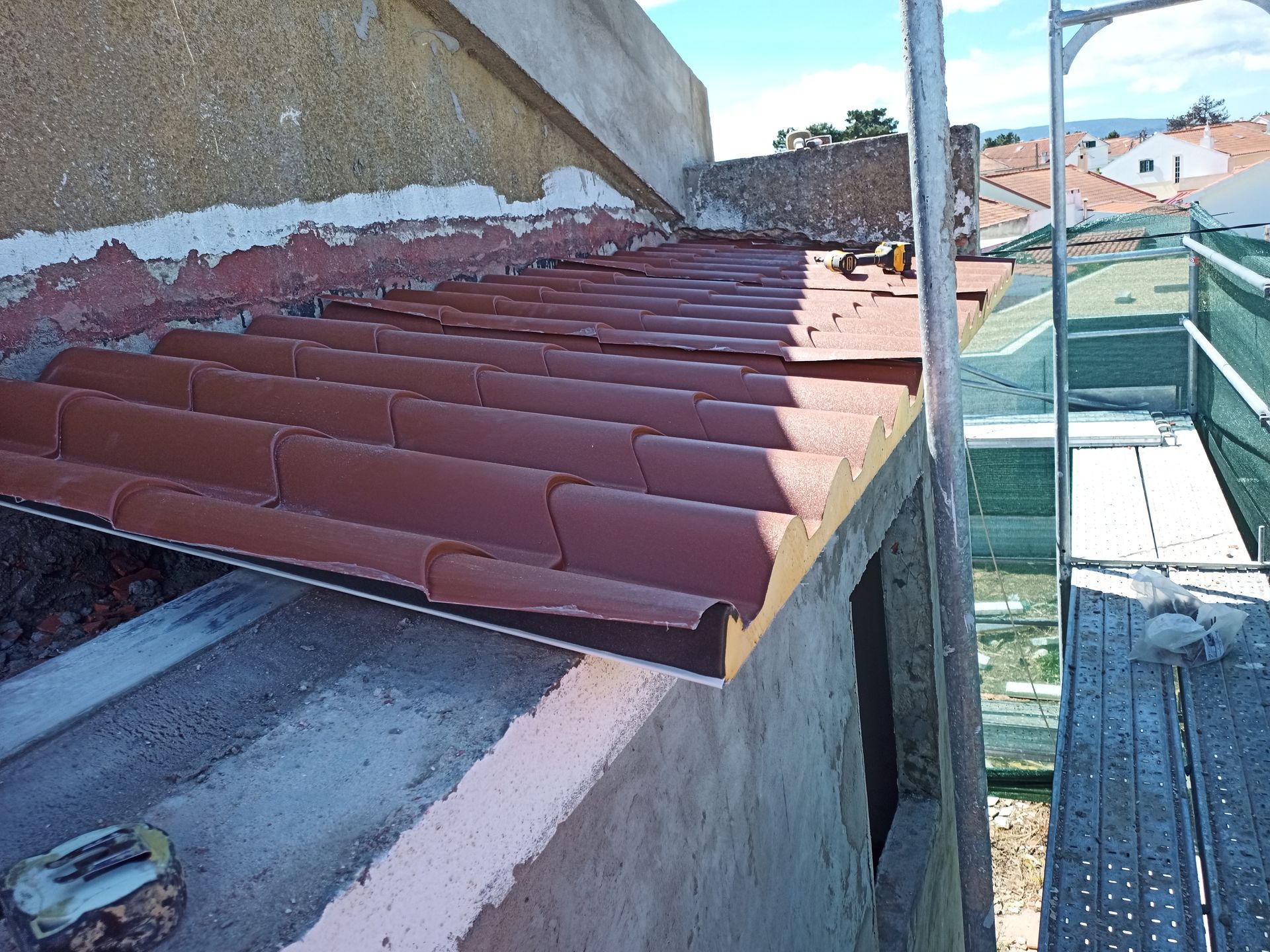 Telhado de telha vermelha em construção; andaimes à direita.