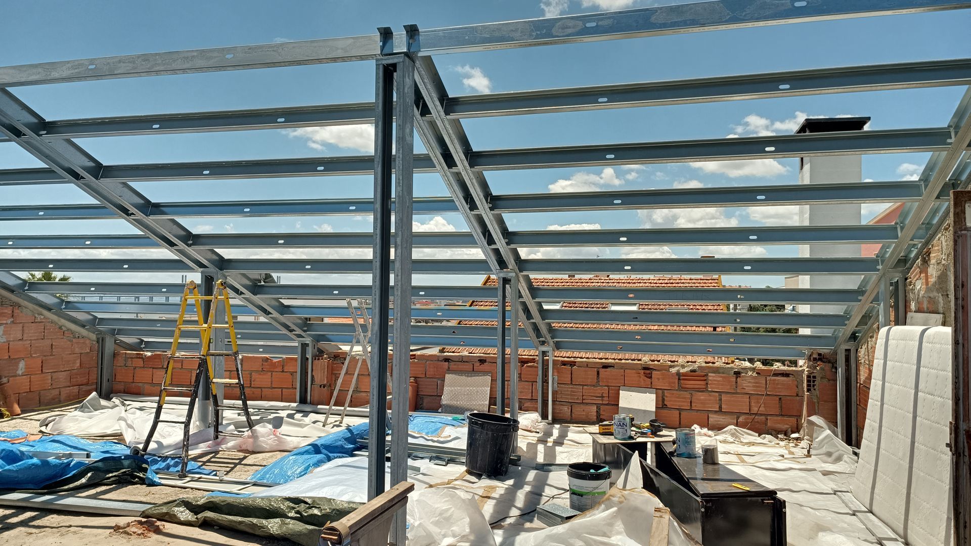 Canteiro de obras com estrutura metálica para o telhado. Interior de um edifício, paredes de tijolo, céu azul.