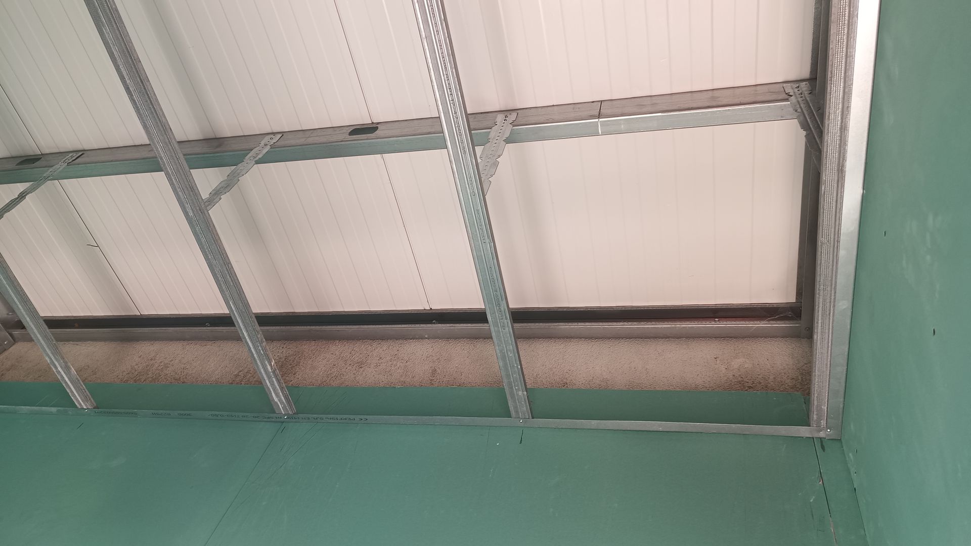 Estrutura do teto: estrutura metálica com painéis, apoiada por vigas contra uma parede verde.