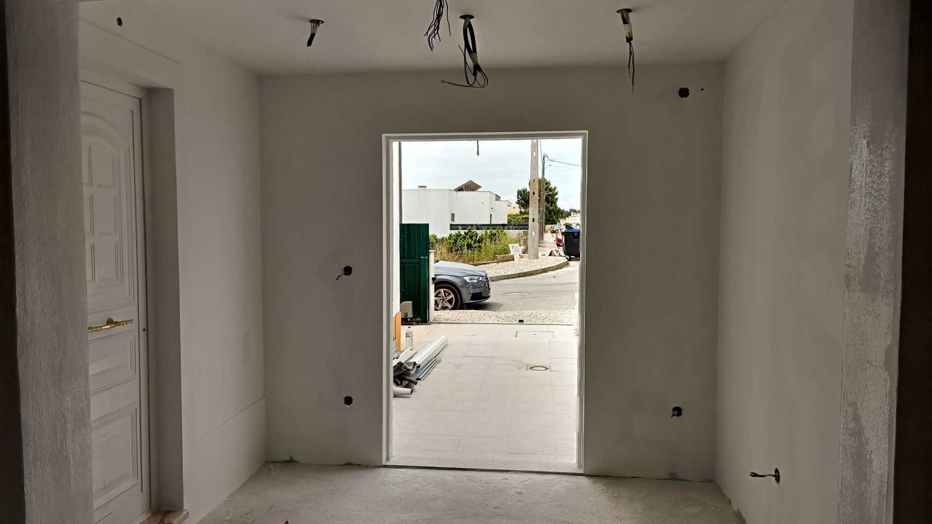 Quarto branco vazio com porta para a rua. Construção inacabada com fiação exposta.