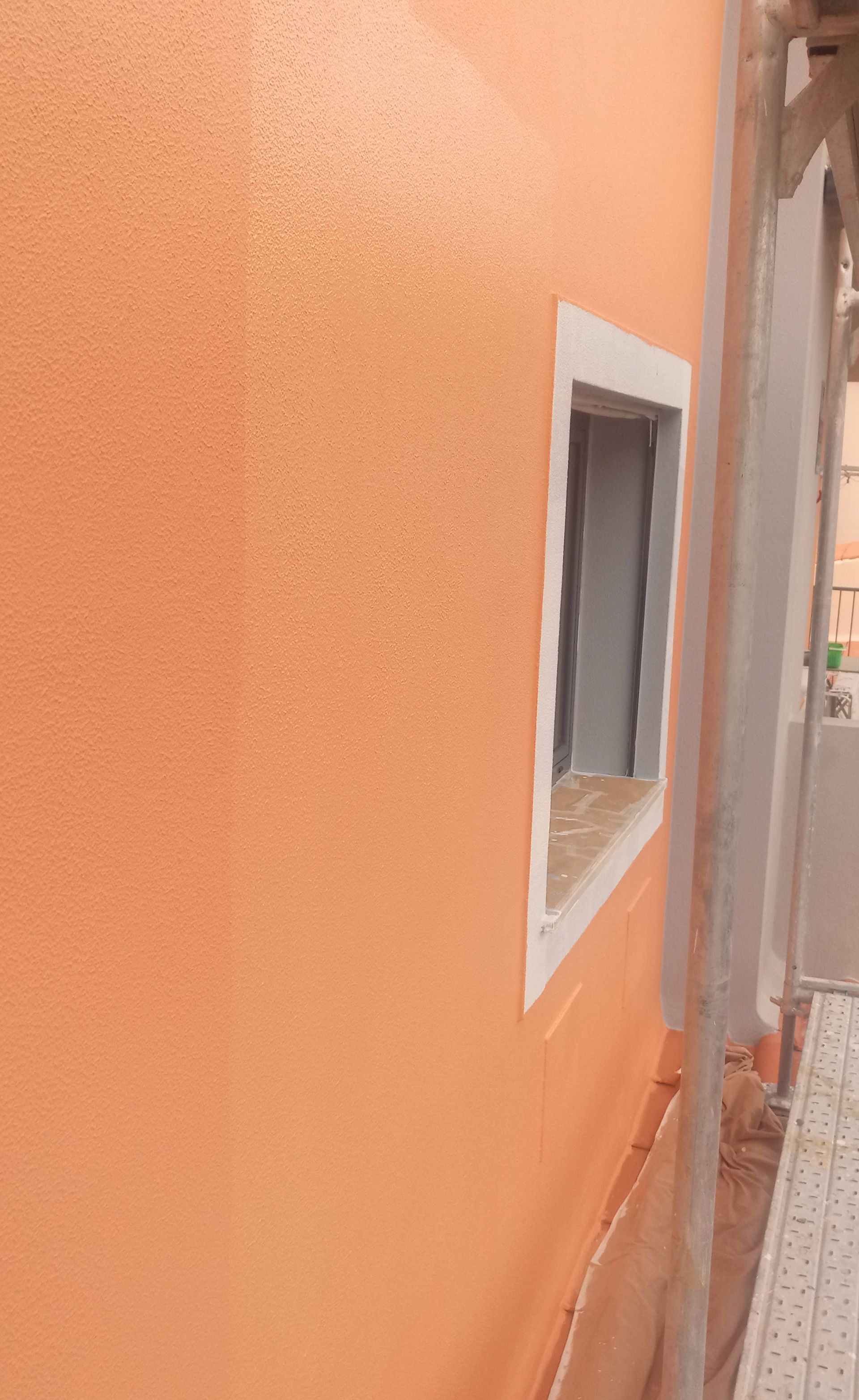 Fachada de edifício em estuque laranja com janela e detalhes em branco.