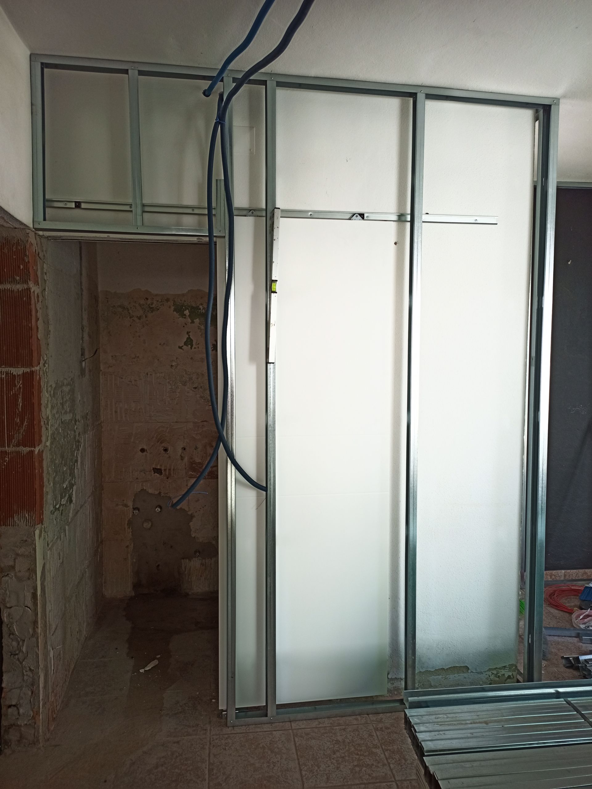 Construção da parede interna em andamento. Estrutura metálica com painéis foscos, abertura para porta.