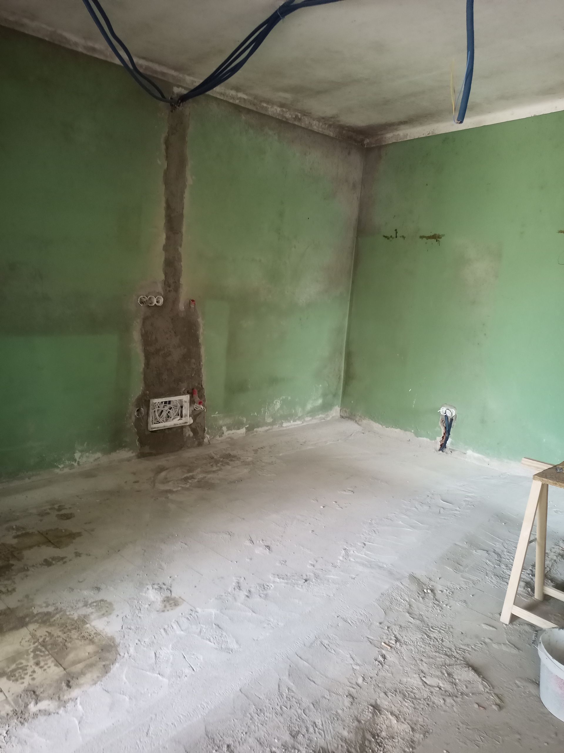 Sala vazia em construção com paredes verdes, piso de concreto e fiação exposta.