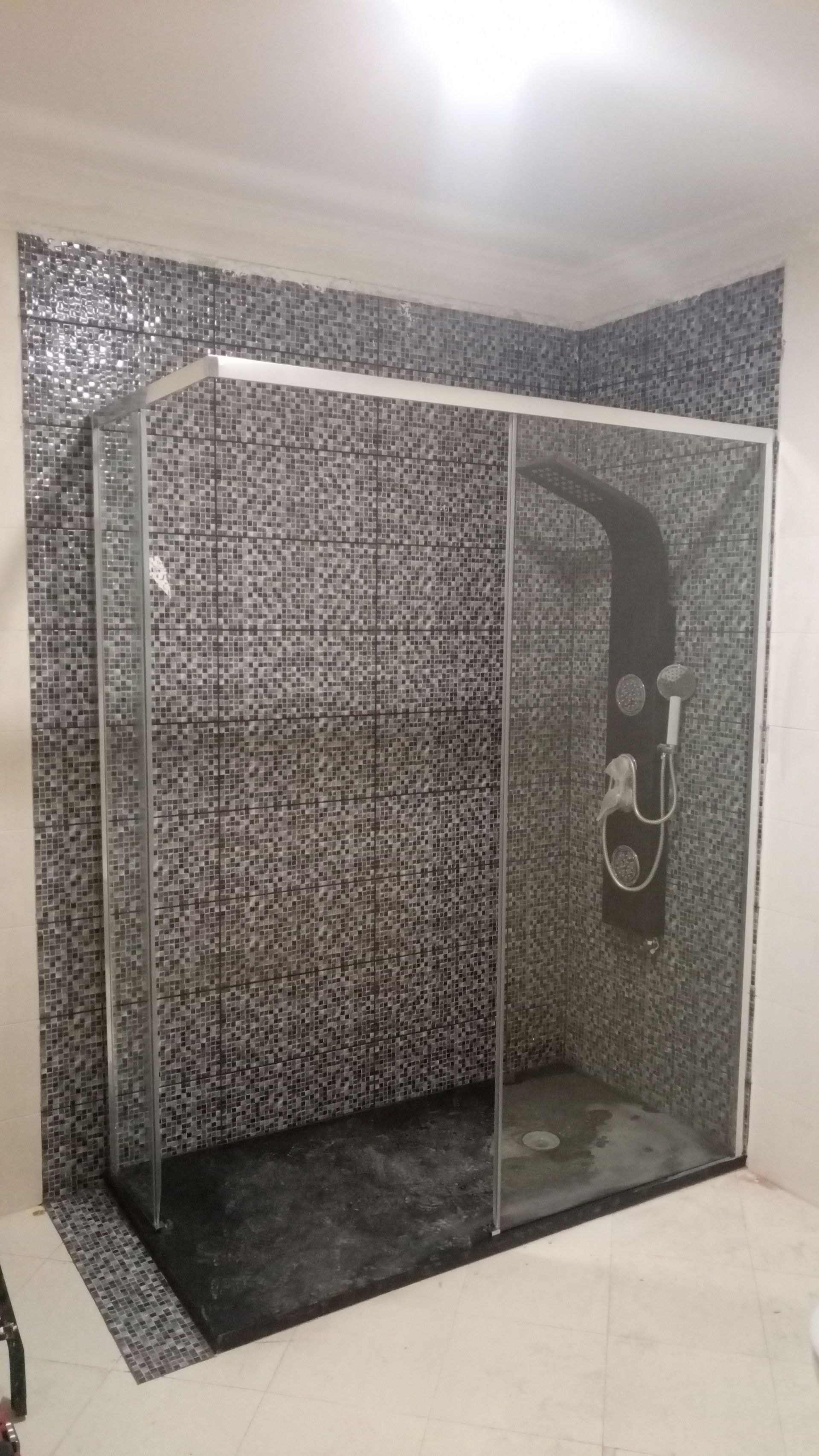 Box de vidro com paredes revestidas com azulejos em mosaico preto e branco e painel de chuveiro preto.