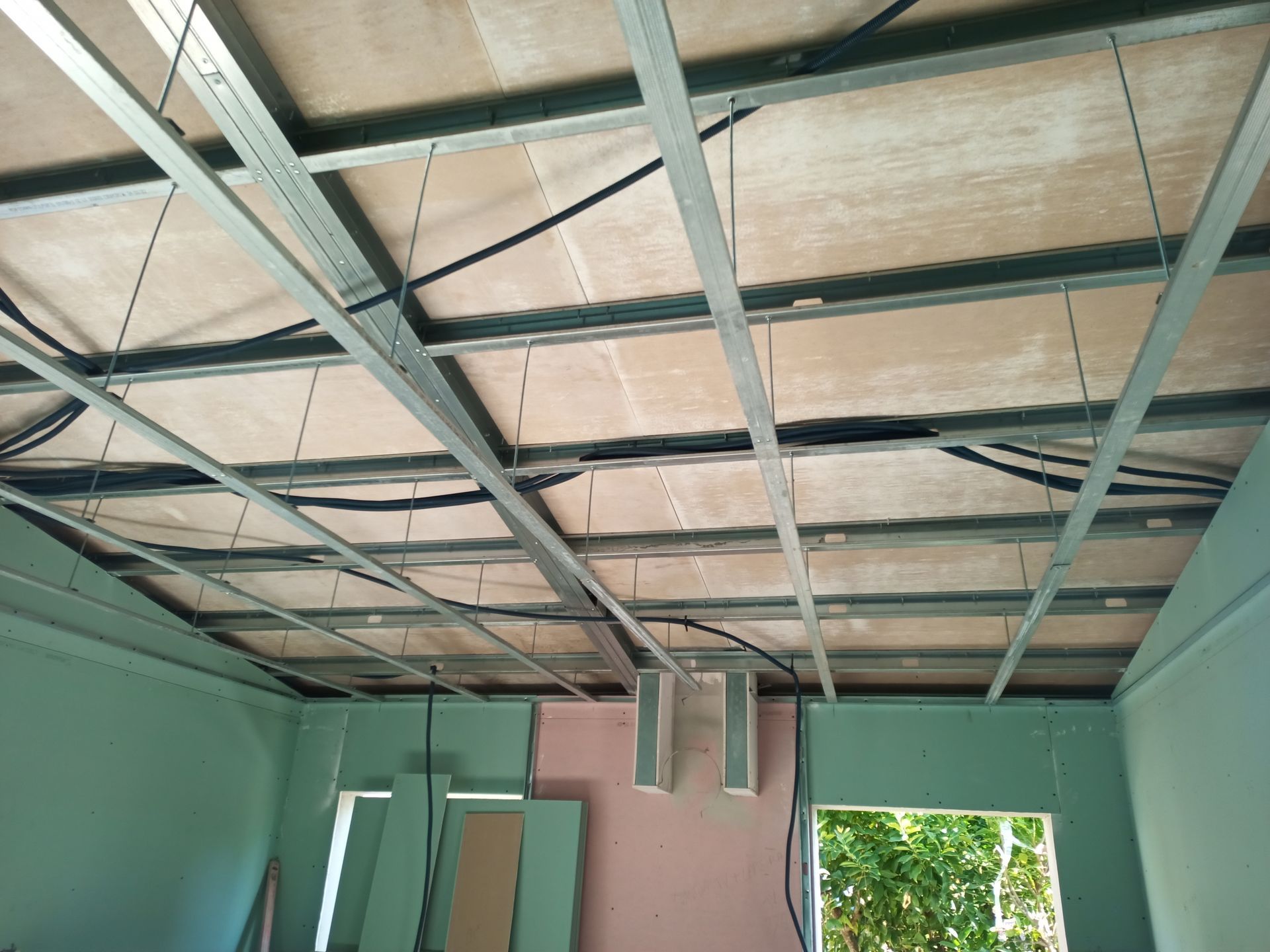 Estrutura do teto em um cômodo, com armação metálica e painéis de isolamento acústico. Há fiação e alto-falantes instalados.