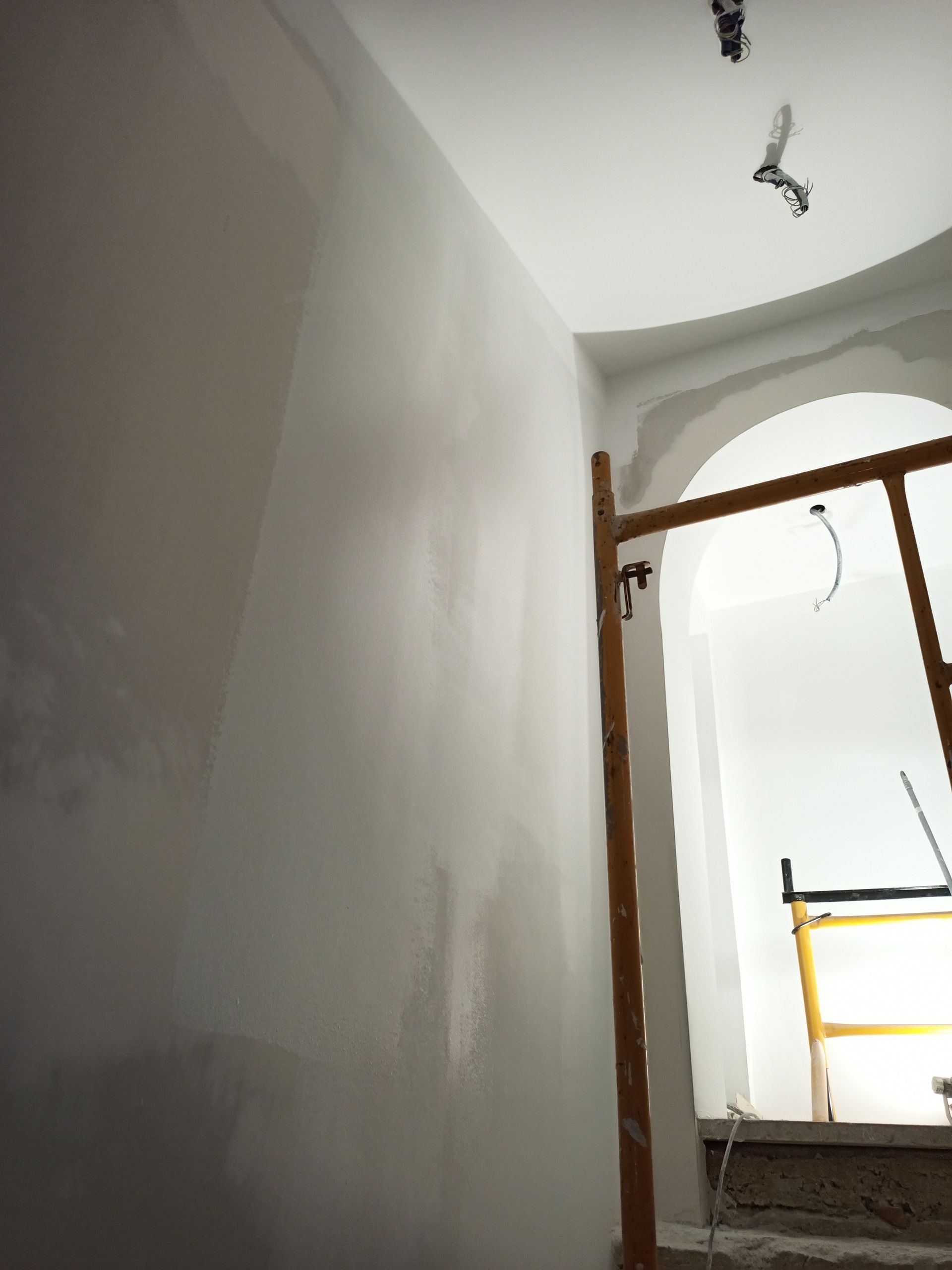 Parede pintada de cinza com porta em arco, andaimes e teto inacabado.