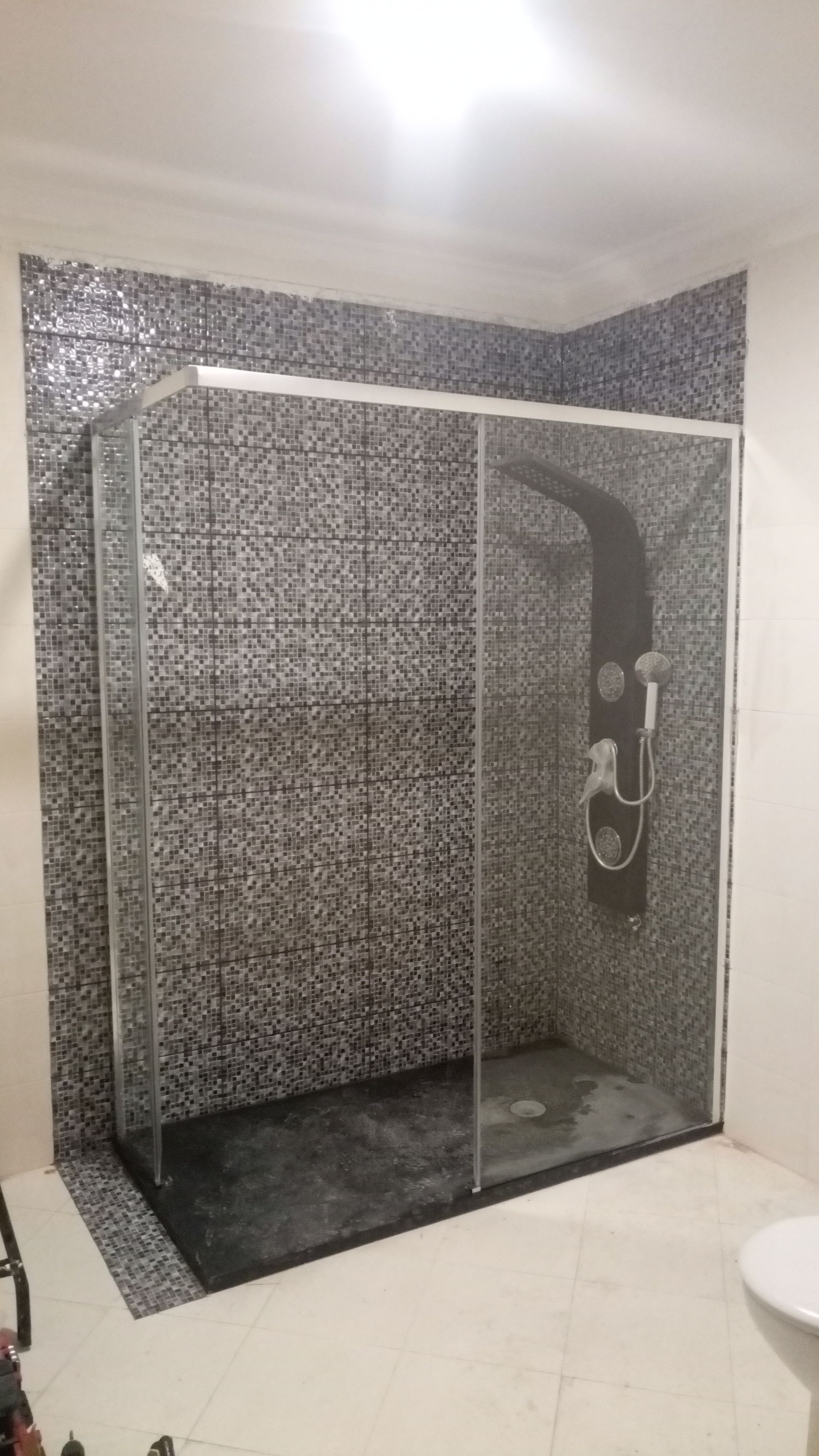 Cabina de duche com paredes revestidas a azulejos de mosaico escuro e painel de duche preto.