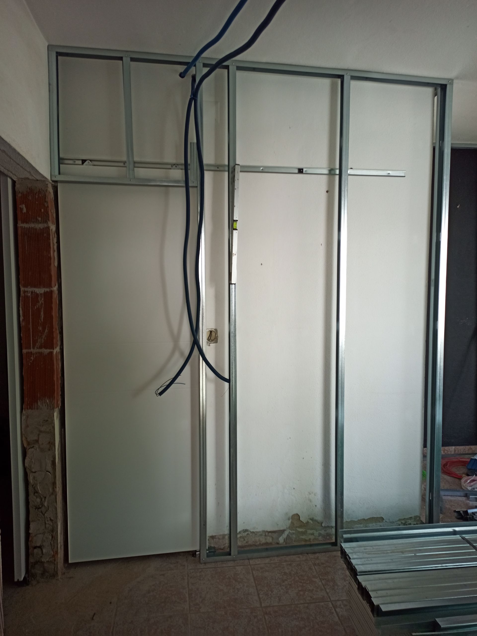 Construção interna: Estrutura metálica para uma parede, com drywall inacabado e fiação elétrica.