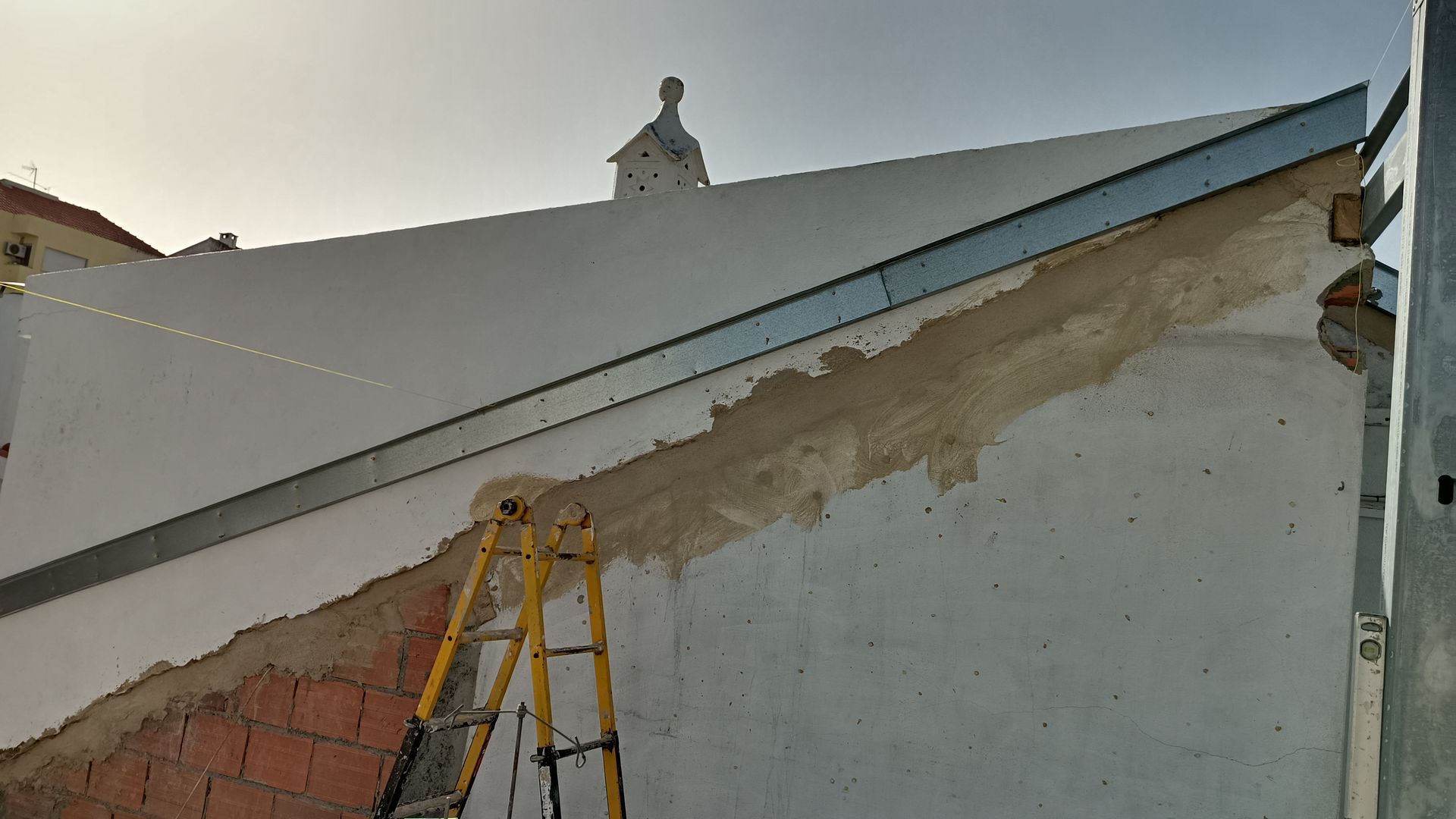 Canteiro de obras: parede branca, tijolo, escada, viga metálica, possivelmente em reforma.