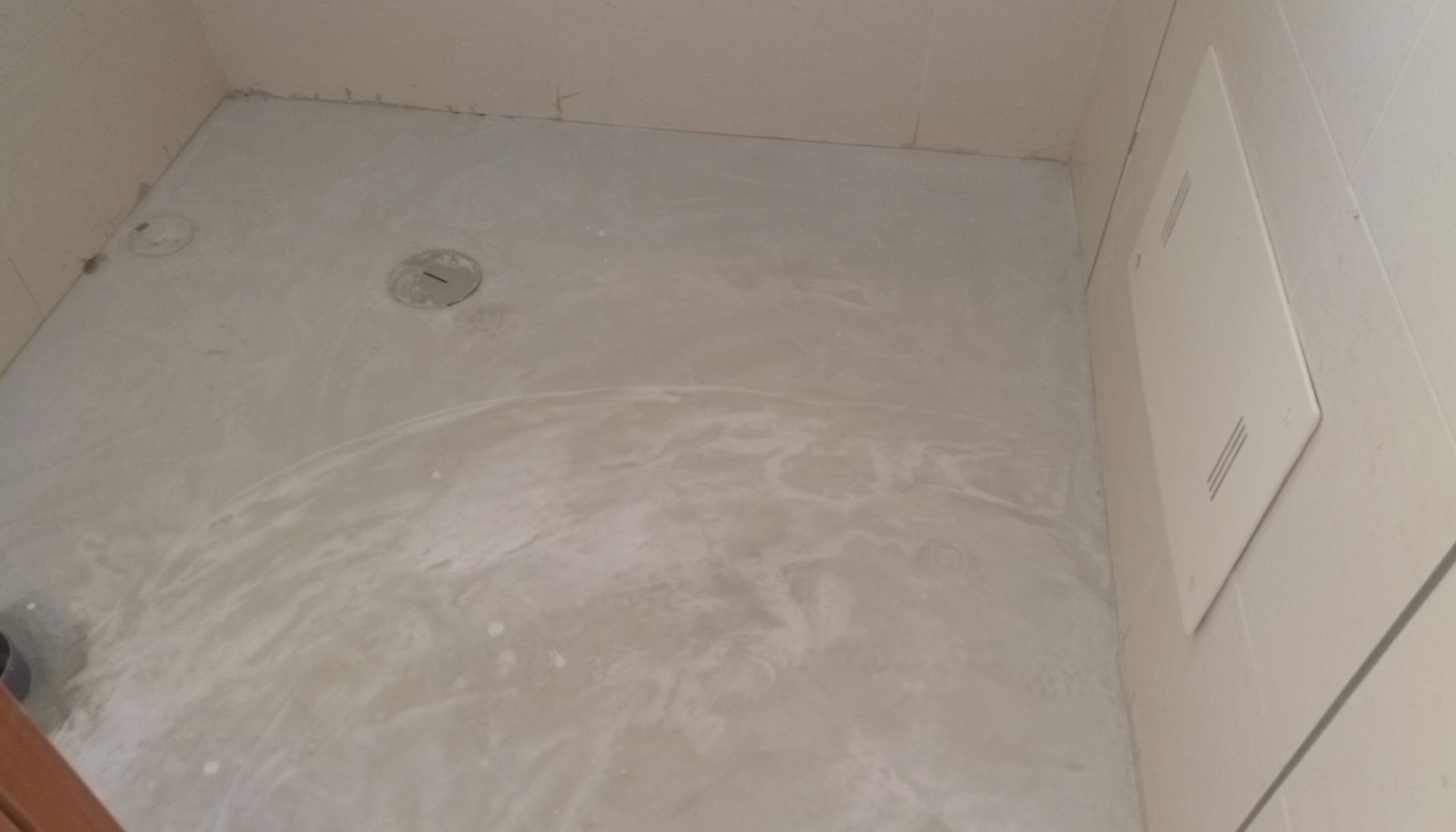 Piso do chuveiro revestido com azulejos brancos e água parada. Ralo no centro, painel na parede da direita.