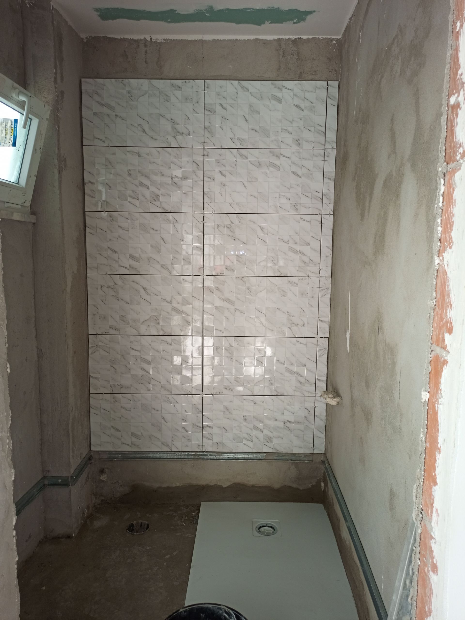 Banheiro em construção; backsplash de azulejos brancos com detalhes metálicos, paredes com acabamento rústico, piso de cimento.