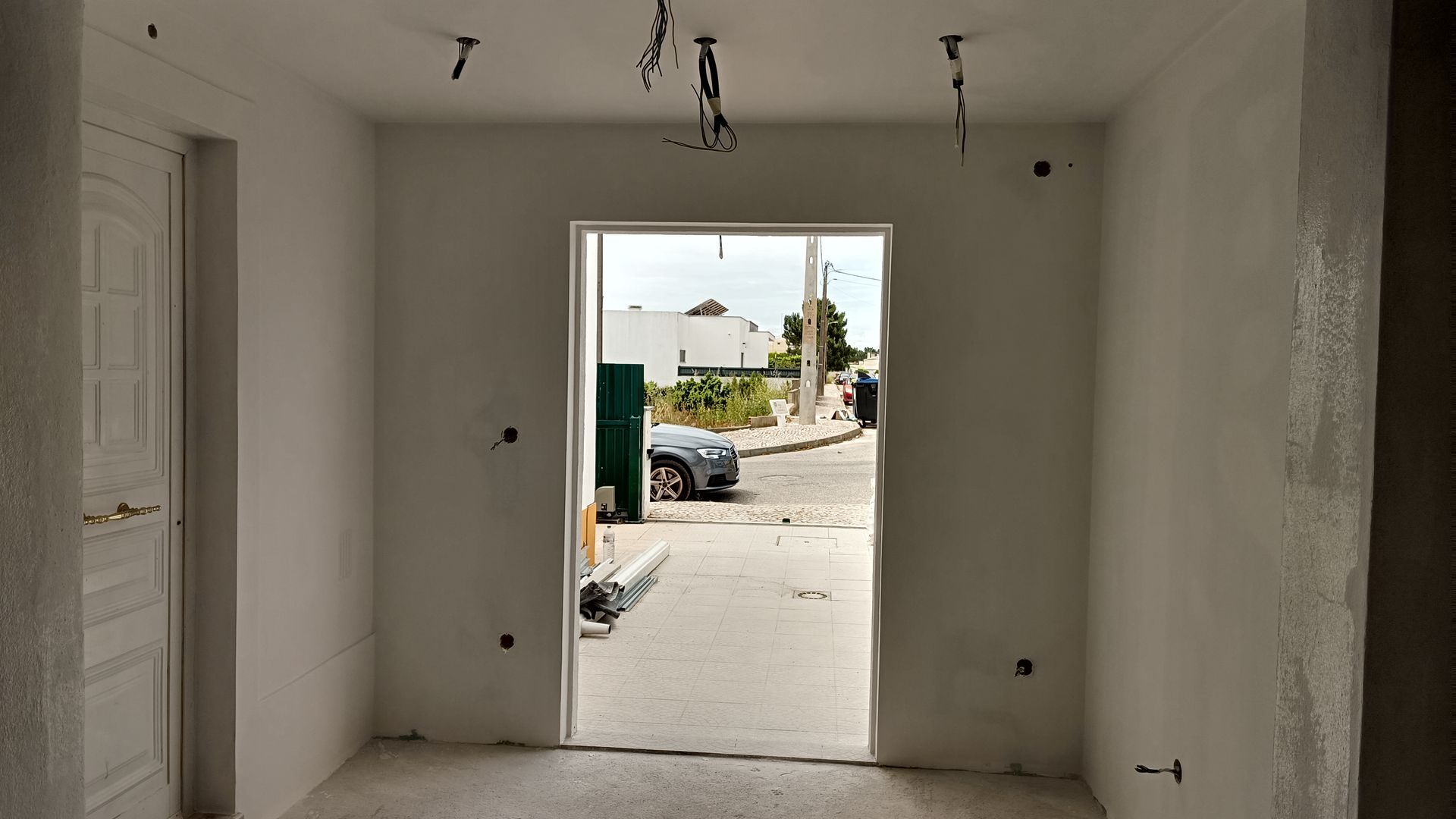 Vista interior de uma sala em construção, com uma porta aberta e fiação no teto.