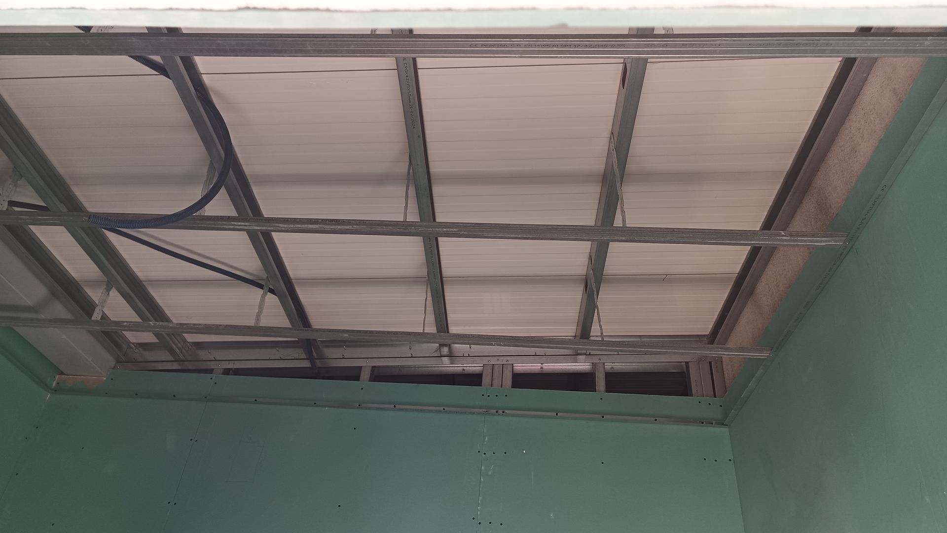 Grelha metálica para teto com painéis retangulares, parcialmente instalada em uma sala com paredes verdes.