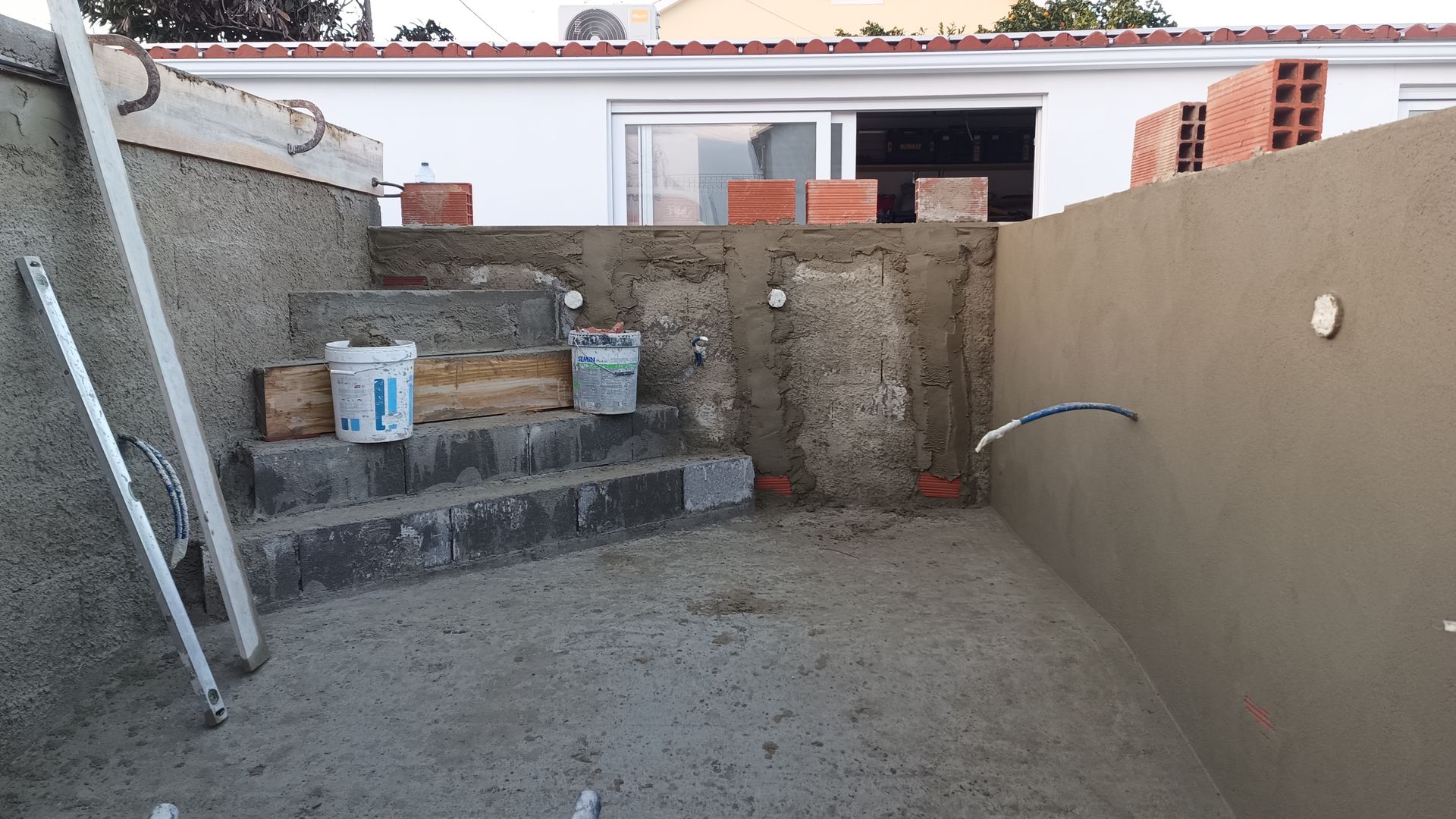 Construção de uma piscina com degraus, paredes inacabadas e materiais de construção.
