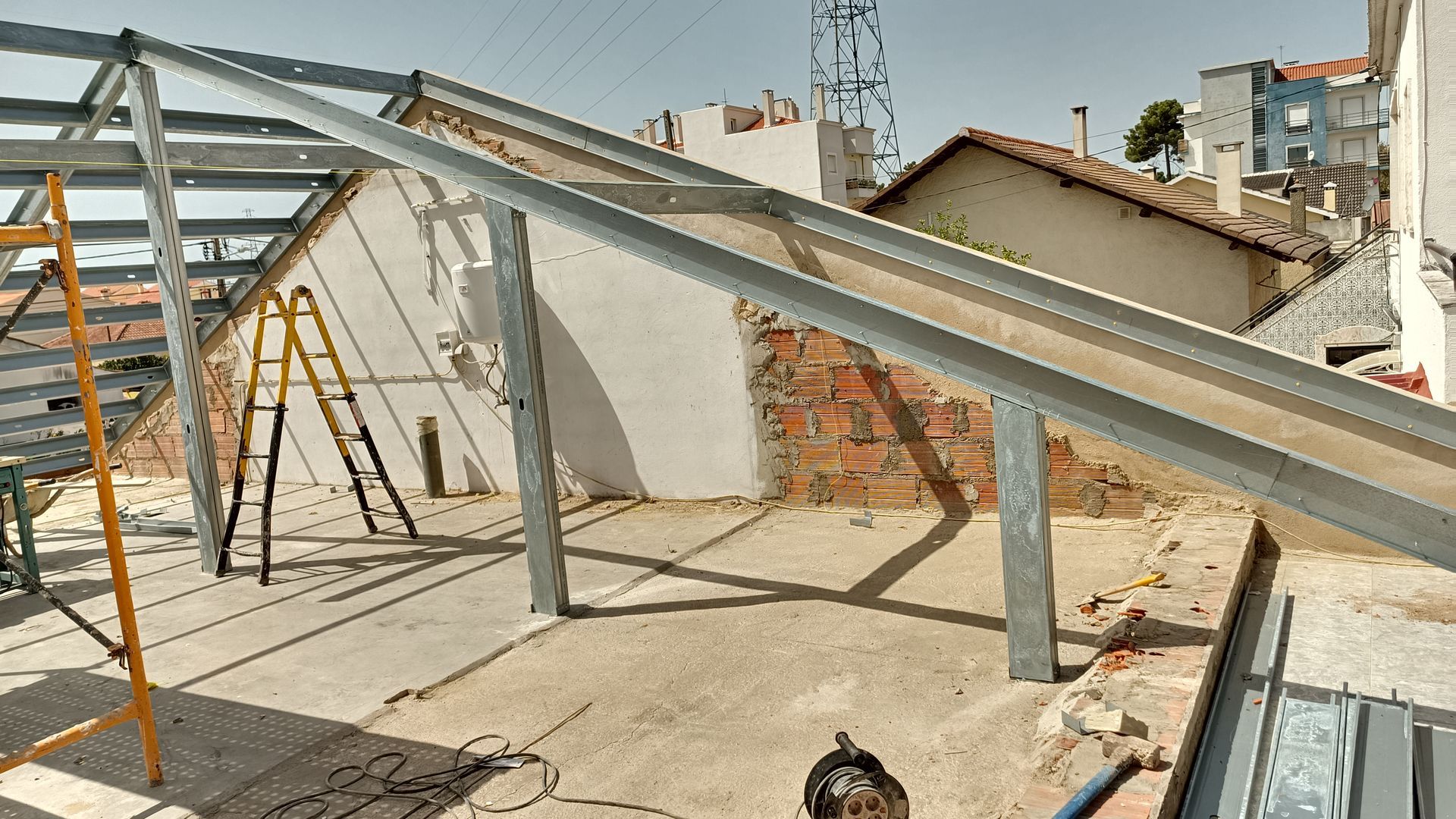 Estrutura metálica em telhado, com parede de tijolos aparentes, andaimes e escada.