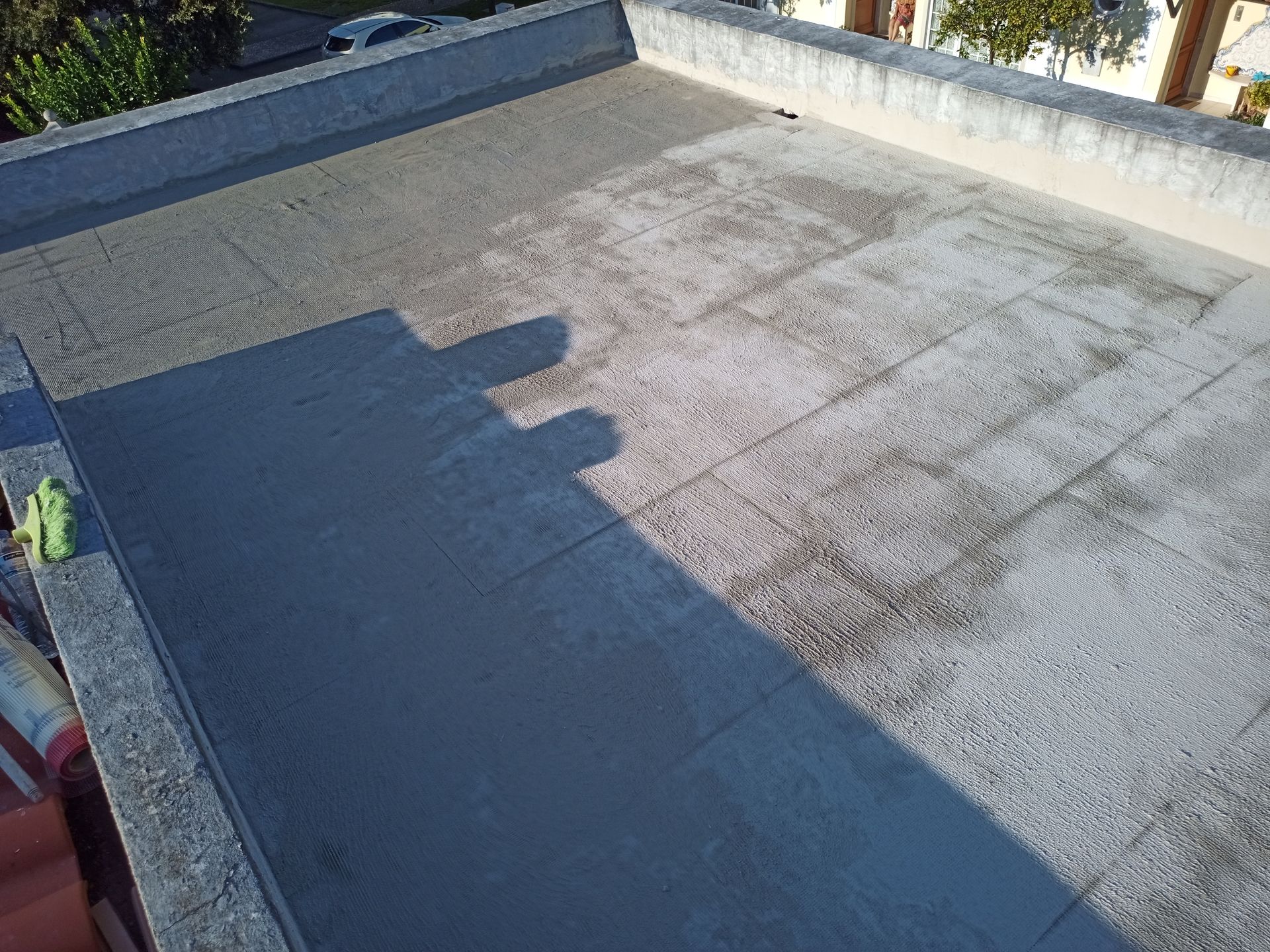 Cobertura plana com revestimento cinza escuro, parcialmente acabada. Borda de concreto circunda a área.