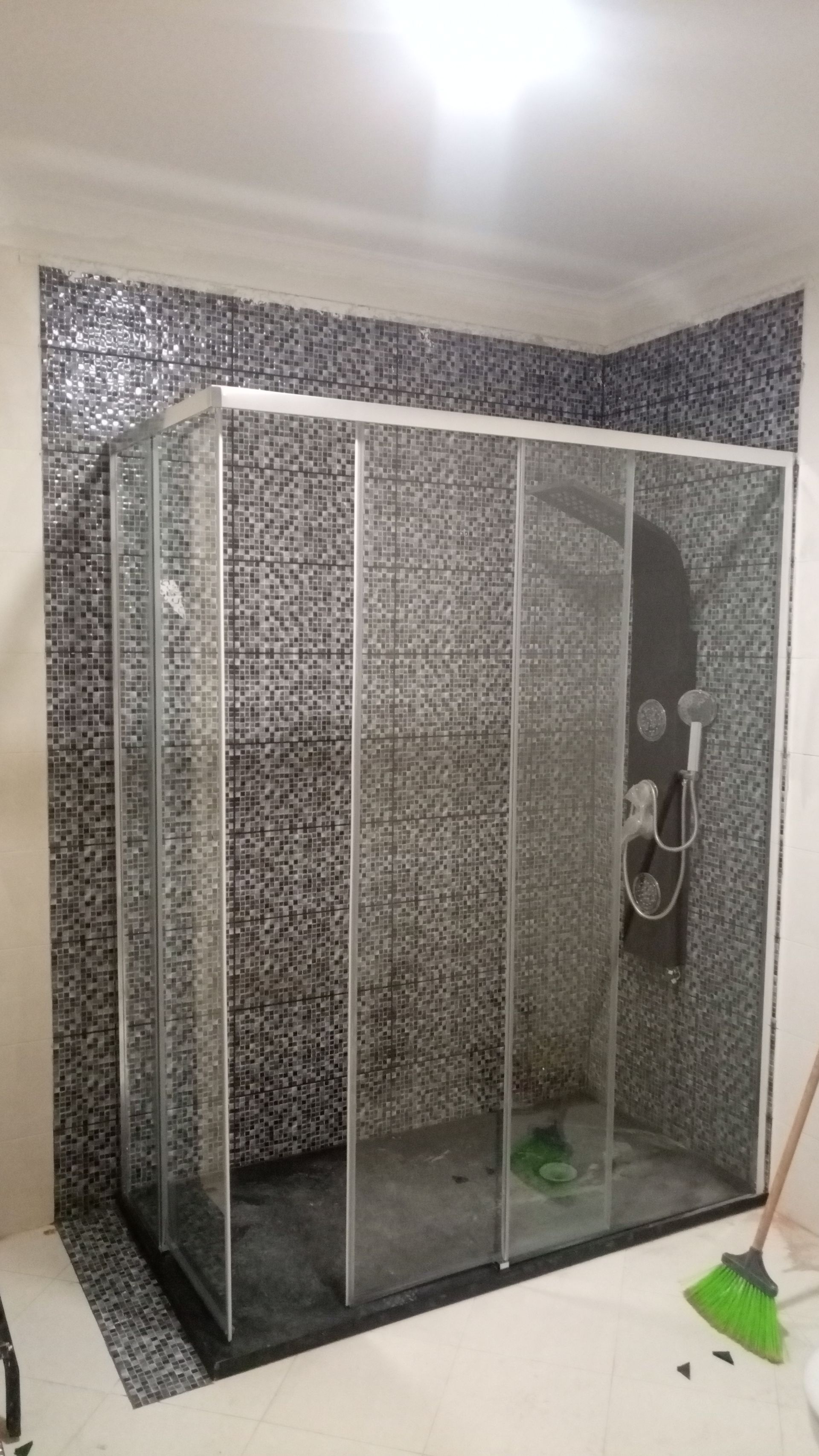 Box de vidro para chuveiro em um banheiro com paredes revestidas com azulejos de mosaico.