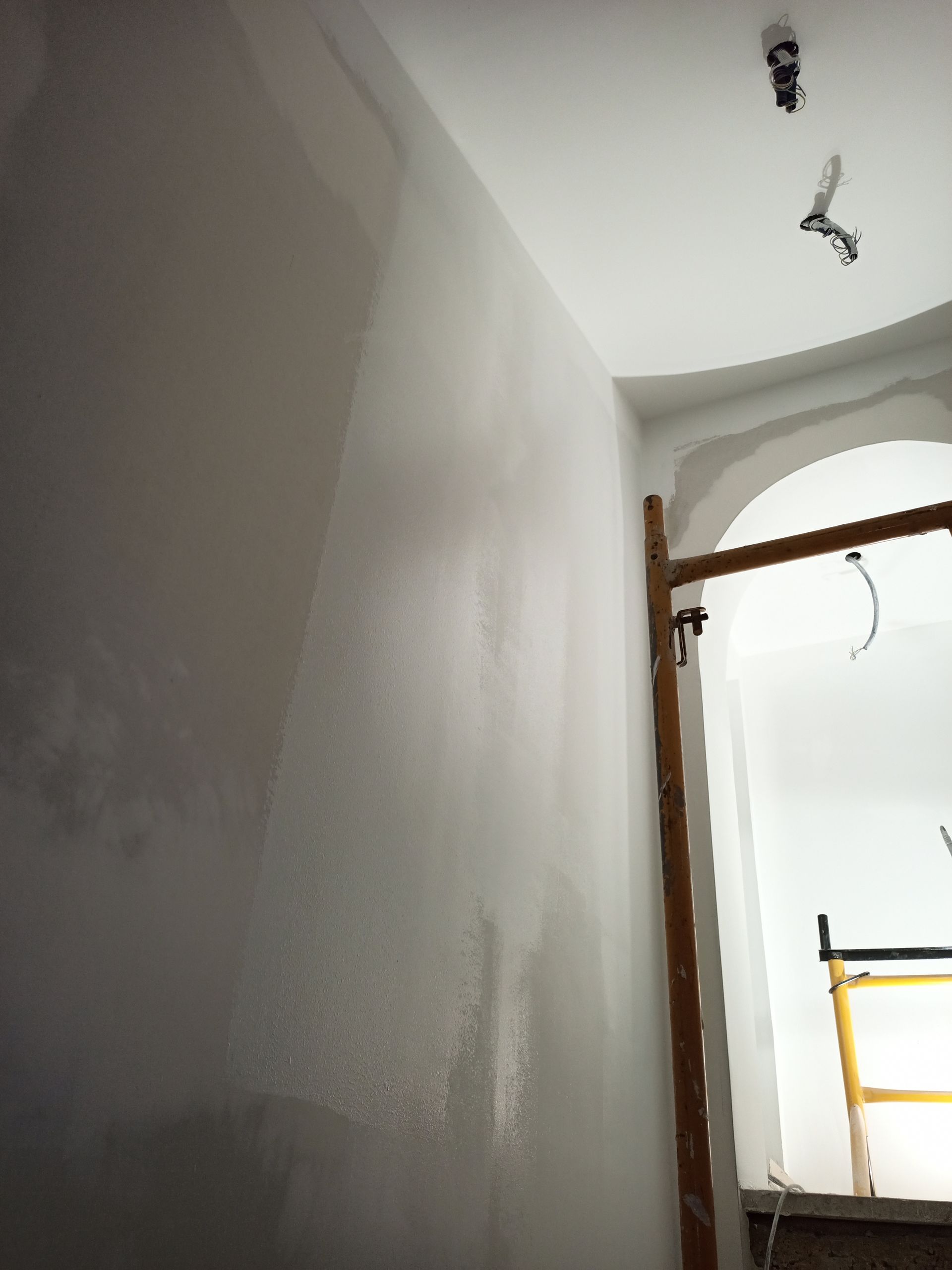 Parede cinza-clara com teto branco, sem acabamento, com escada visível.