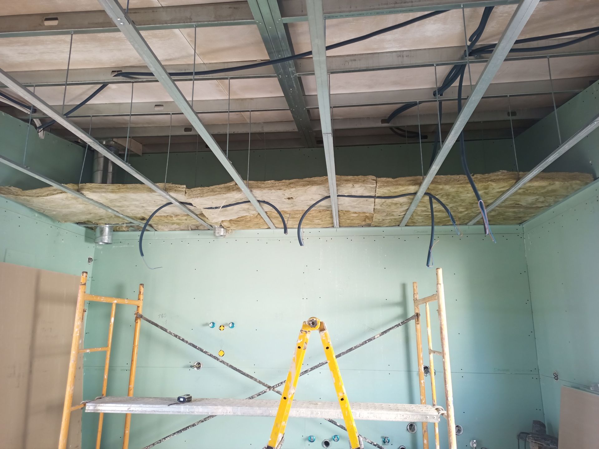 Construção interna: Isolamento e estrutura metálica instalados em um cômodo. Andaimes visíveis.