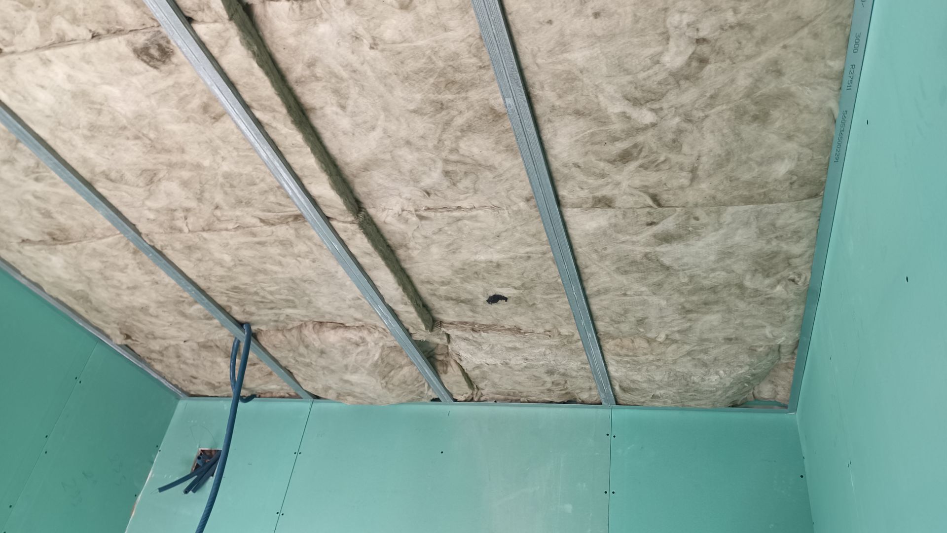 Teto em construção com isolamento entre suportes metálicos. Paredes turquesa.