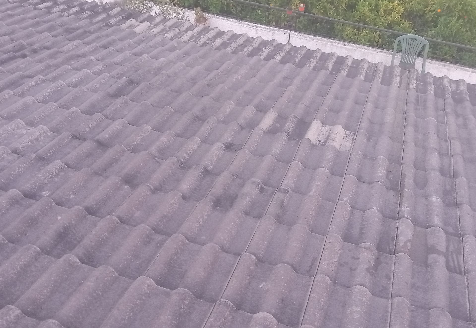Telhado de telhas cinzentas com aspecto desgastado e uma cadeira verde na beirada.