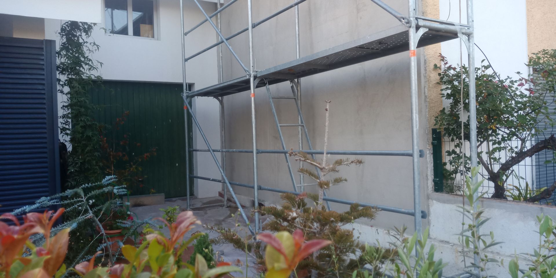 Andaimes ao lado de um prédio com uma porta verde e folhagem em primeiro plano.
