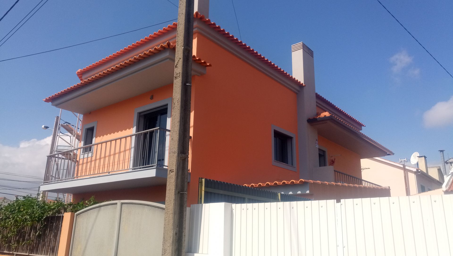 Casa laranja de dois andares com chaminé cinza e telhado de telhas vermelhas, varanda com balaustrada ornamentada.