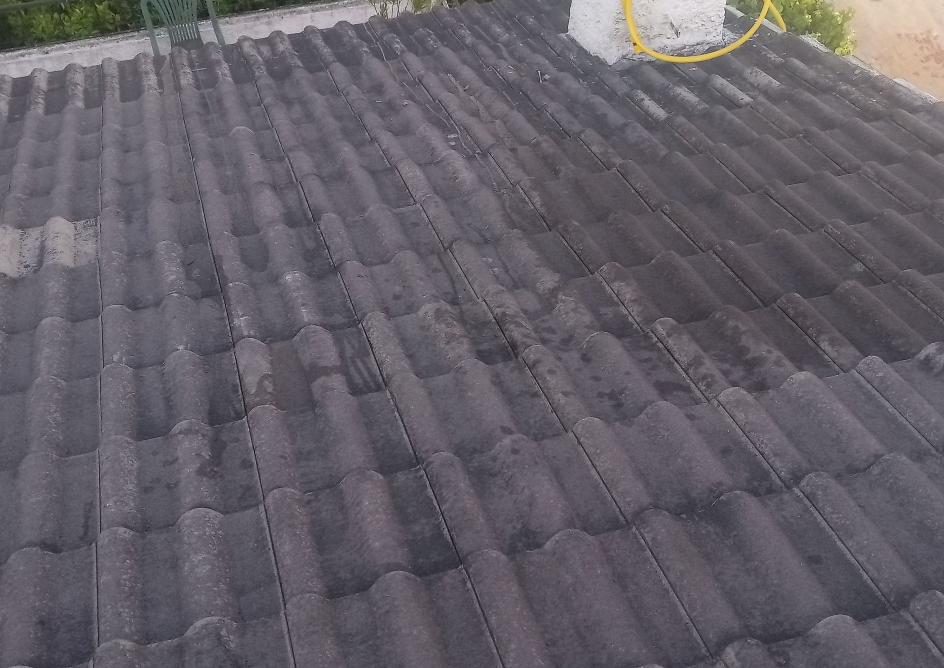 Telhado escuro e desgastado com textura visível, chaminé e mangueira amarela.