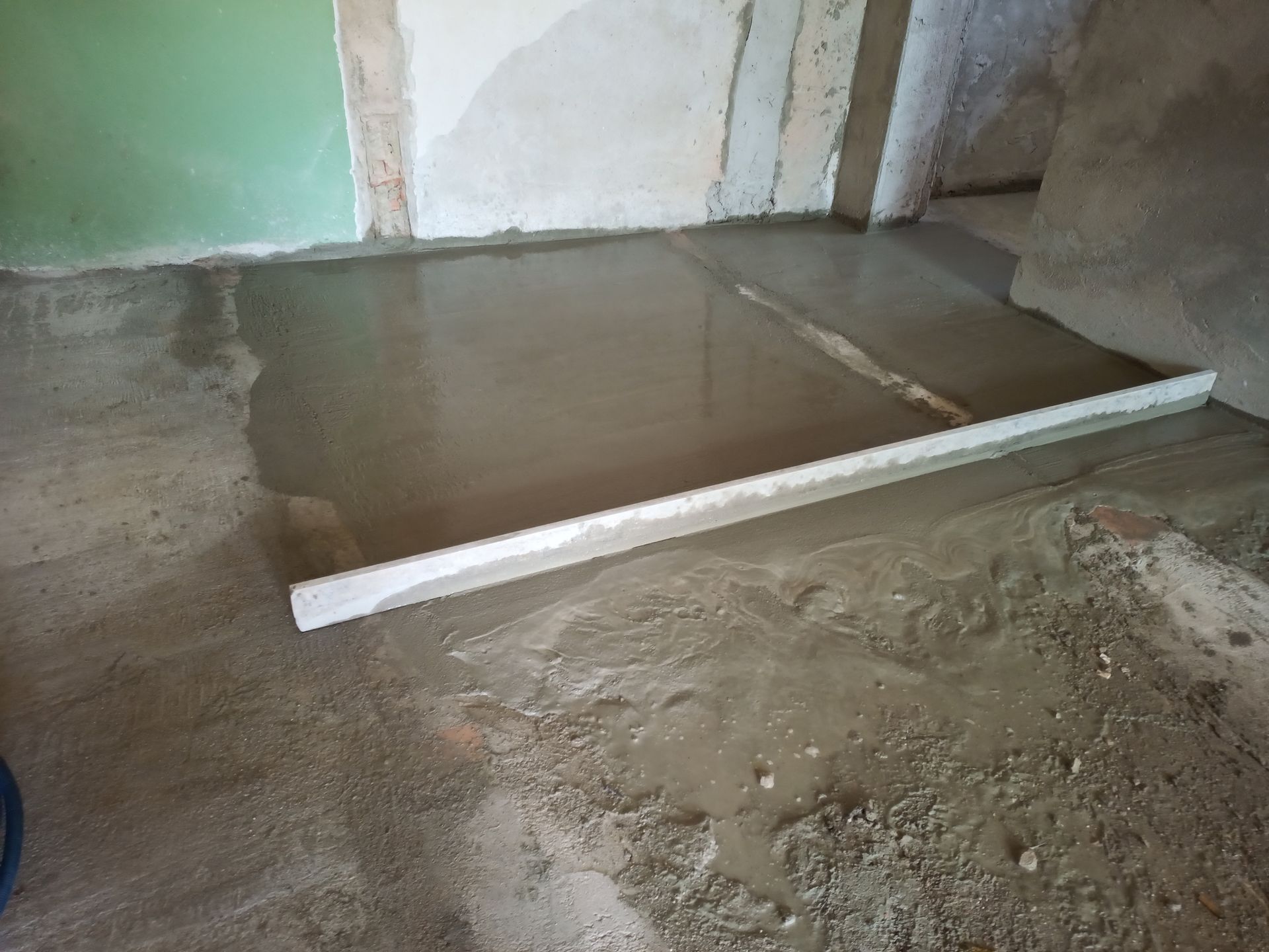Concreto fresco sendo nivelado com uma régua em uma sala com paredes parcialmente acabadas.