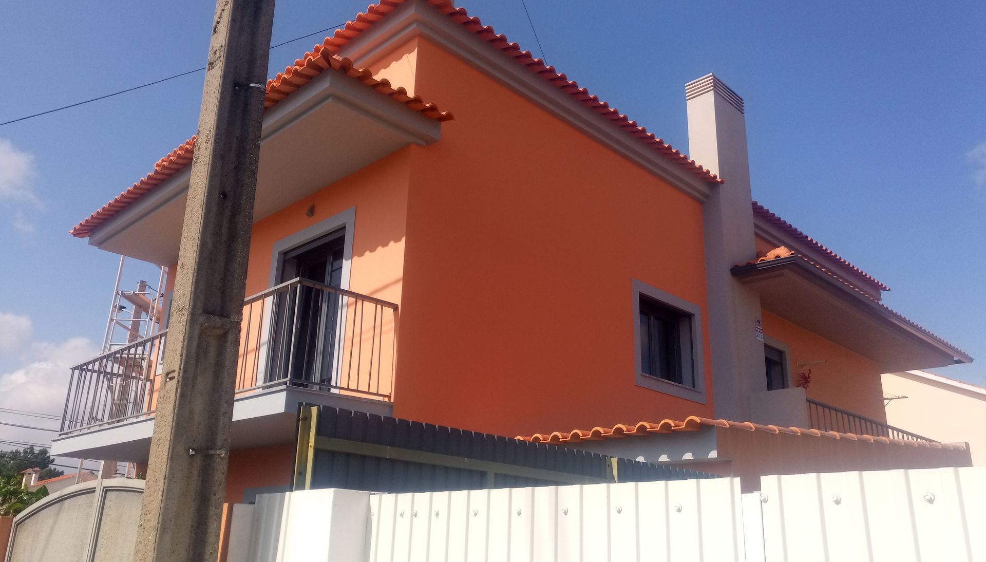 Casa laranja de dois andares com varandas, telhado de telha vermelha e chaminé contra um céu azul.