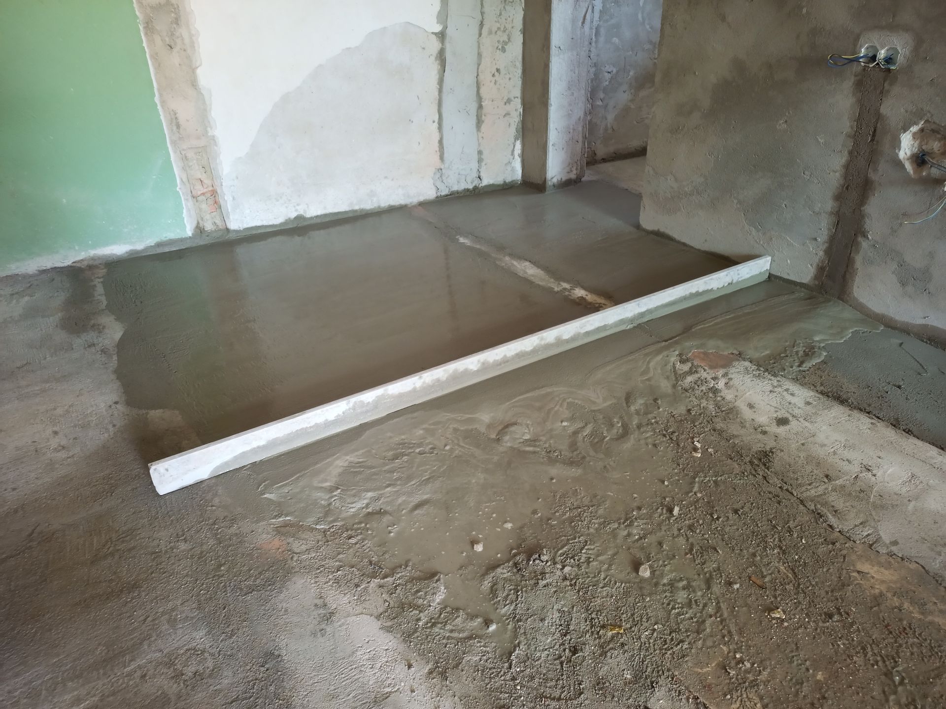 Piso de concreto fresco sendo nivelado com uma régua longa em uma sala em construção.