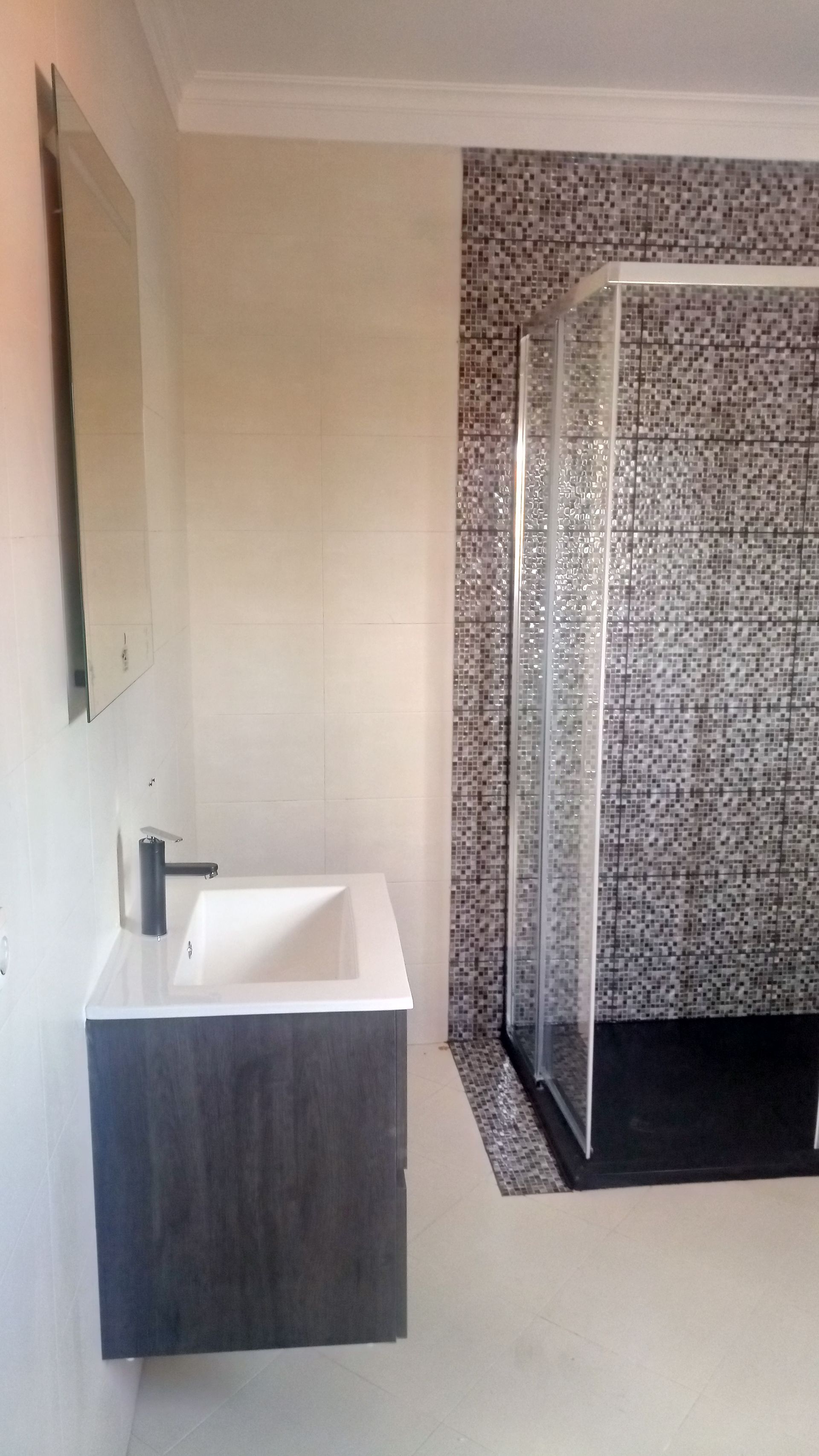 Banheiro moderno com pia, espelho e box de vidro com azulejos em mosaico preto e branco.