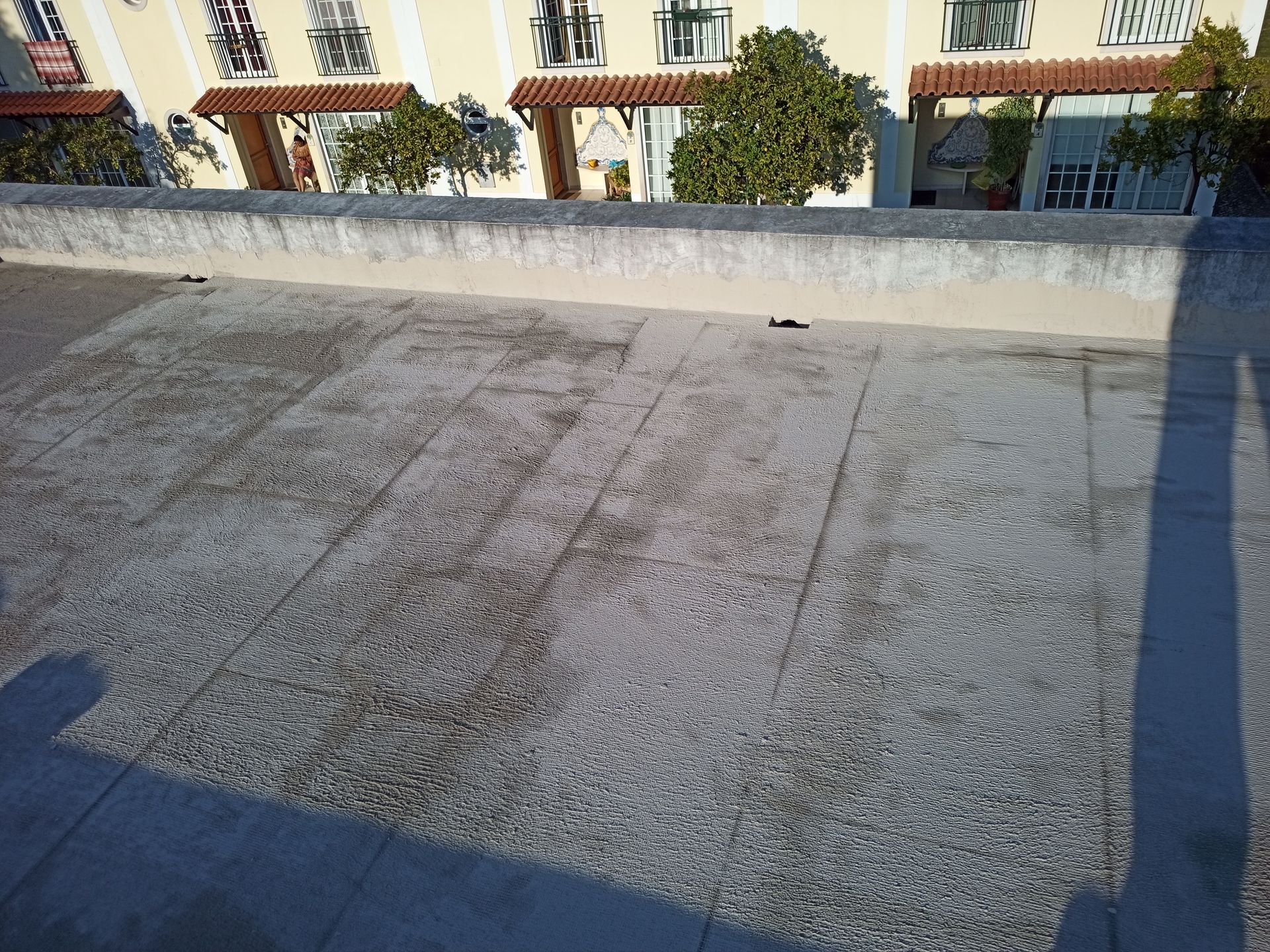 Cobertura de concreto com um muro baixo, em frente a um prédio com paredes bege e telhado de telhas vermelhas.