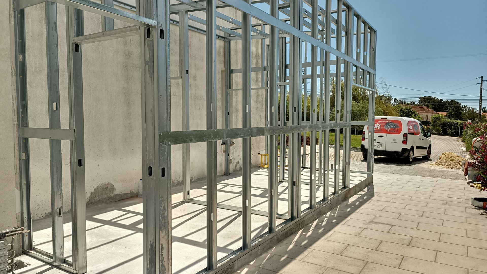 Estrutura metálica de uma construção em andamento ao ar livre, com um veículo branco visível.