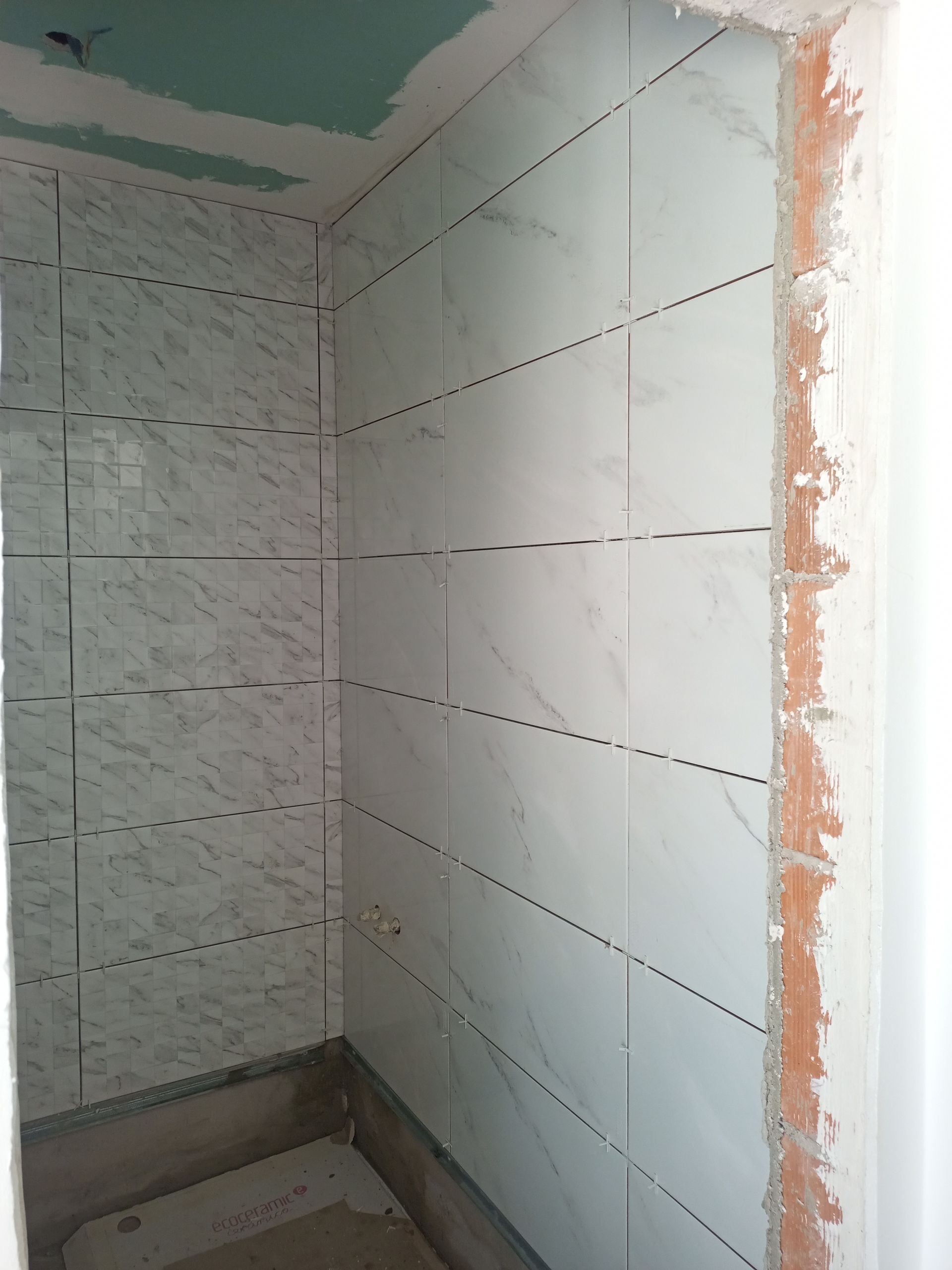 Paredes do banheiro revestidas com azulejos brancos com aparência de mármore. As linhas pontilhadas indicam o rejunte; parede da direita sem acabamento.