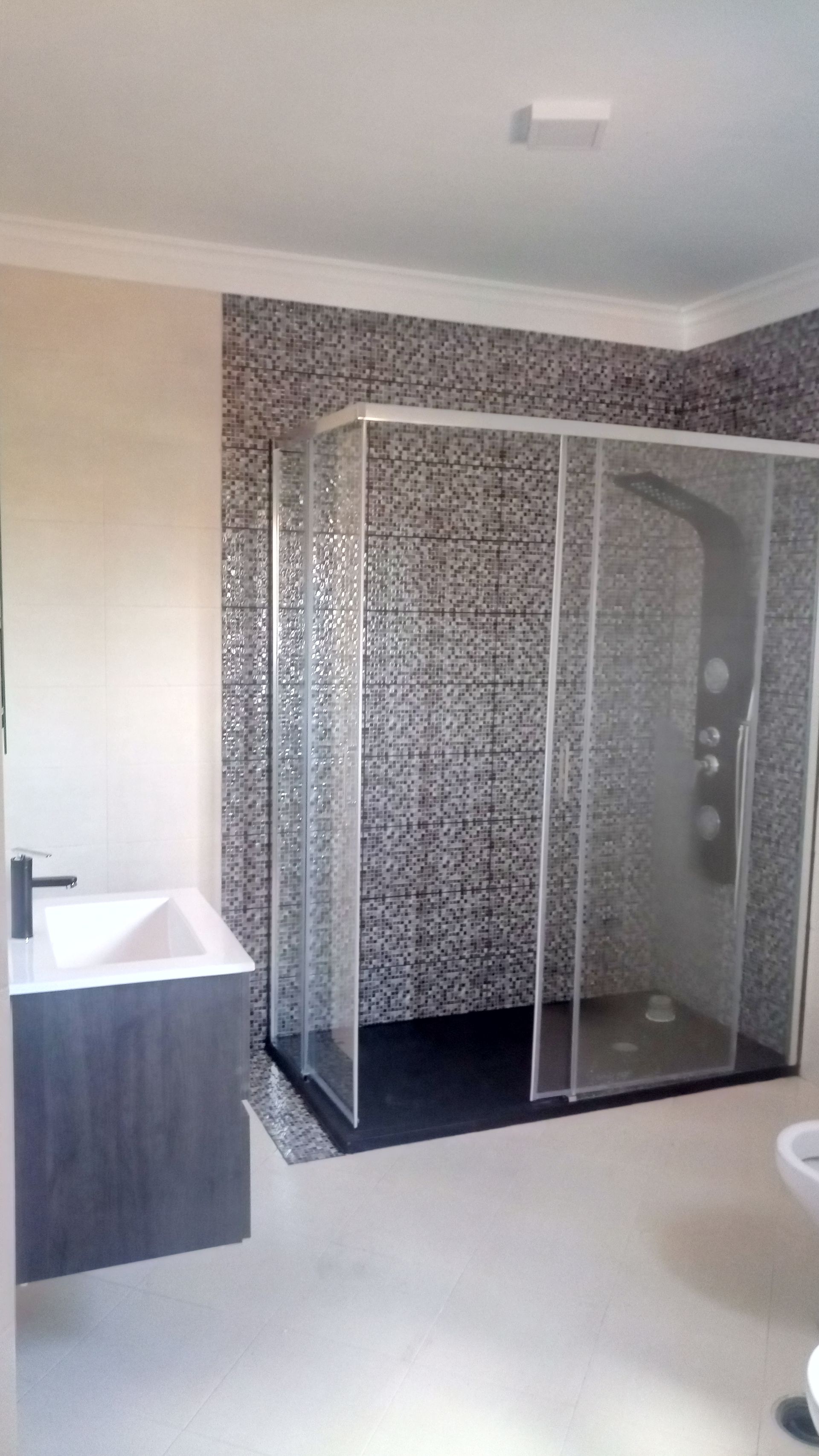 Banheiro moderno com box de vidro, parede revestida com azulejos em mosaico e pia com bancada.