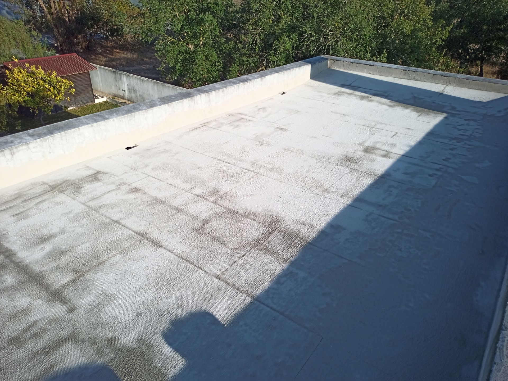 Cobertura plana de concreto com superfície de cor clara, áreas sombreadas e muro baixo circundando o perímetro.