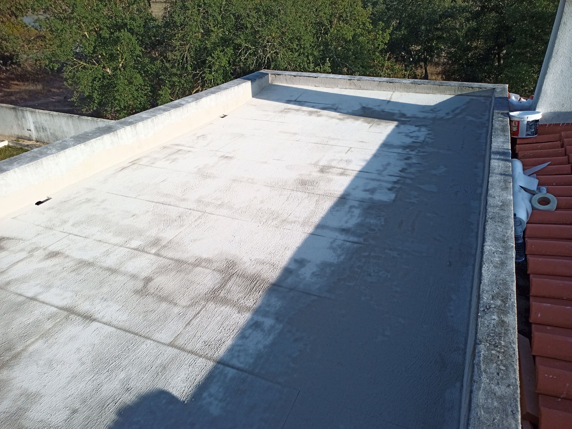 Telhado plano com revestimento cinza claro e mancha cinza escura, cercado por um muro baixo.