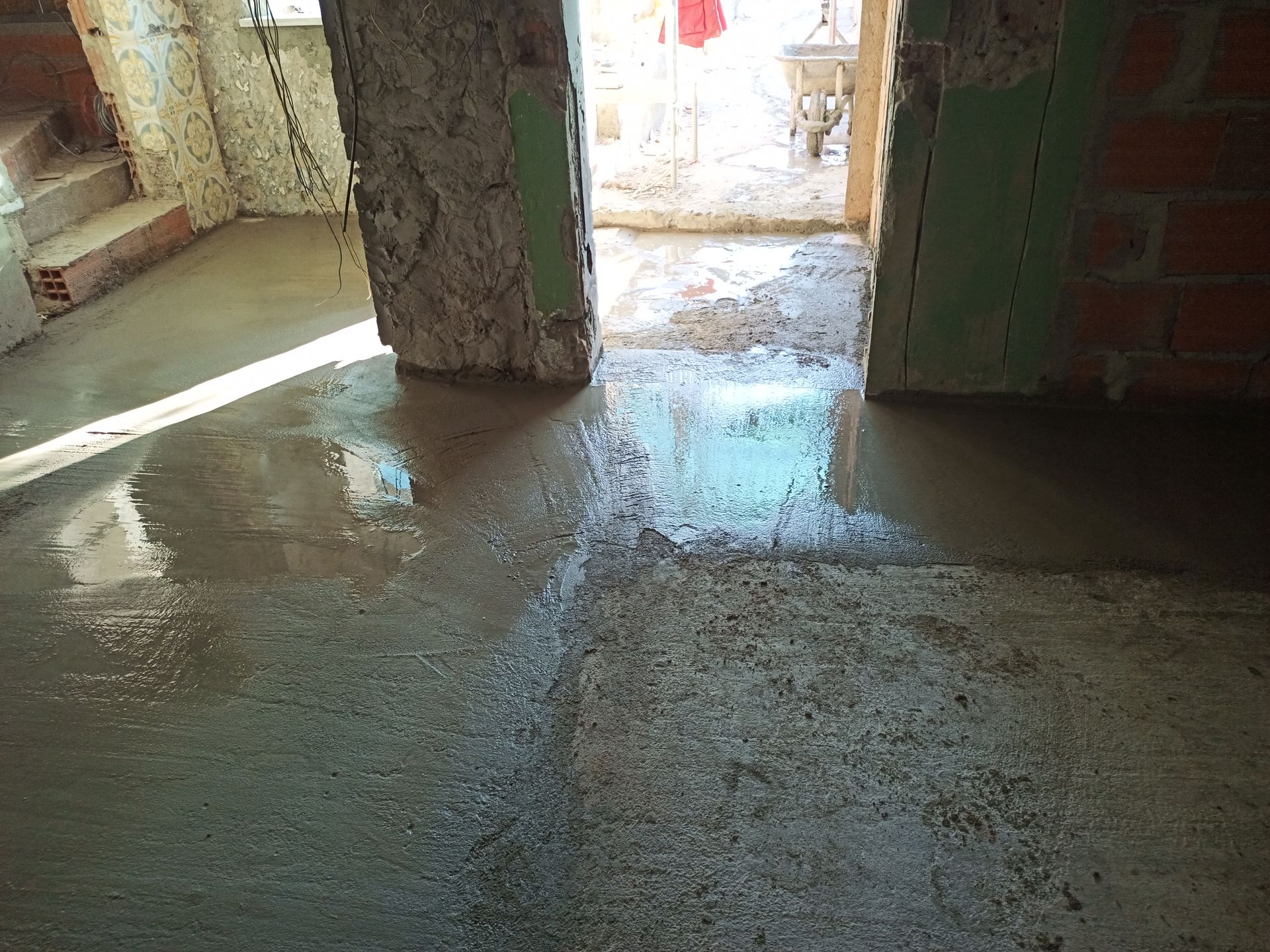 Piso de concreto recém-colocado em uma sala com portas e paredes de tijolos aparentes, ainda úmido.