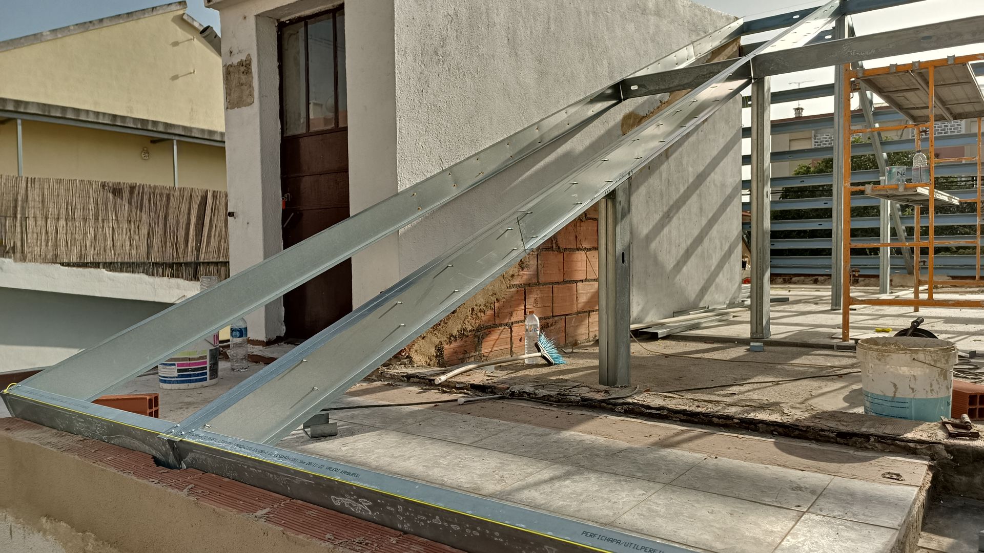 Estrutura metálica de um telhado em construção no topo de um edifício, perto de uma porta e de uma parede de tijolos.