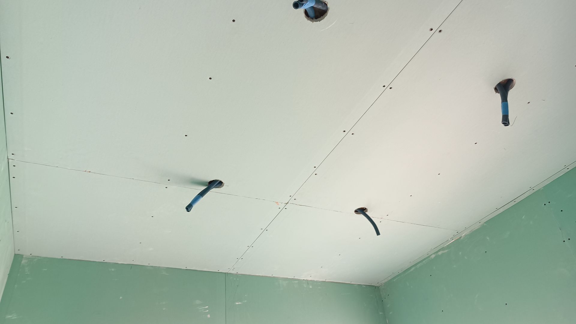 Teto de gesso cartonado verde com fios elétricos azuis expostos em um cômodo.