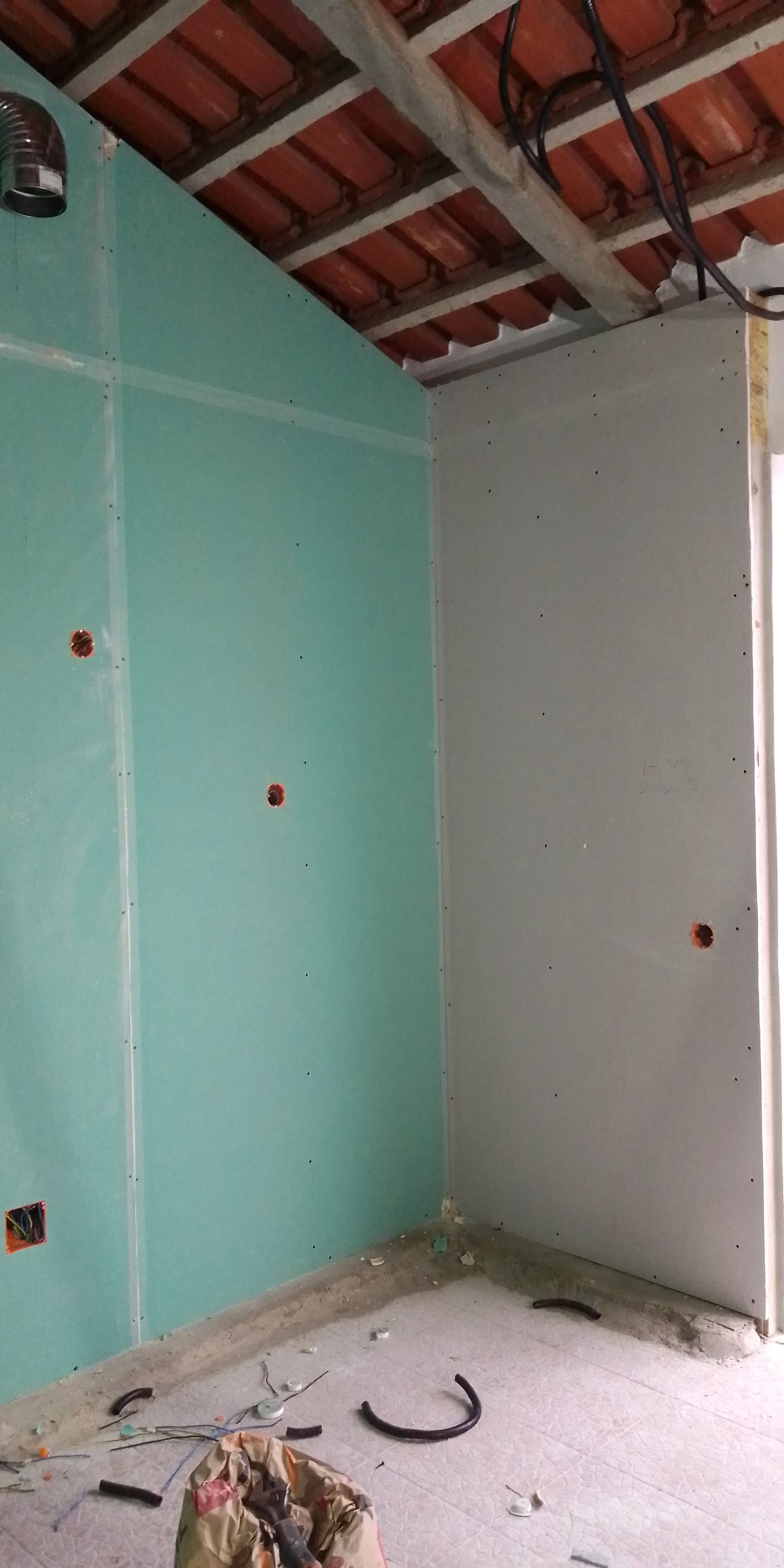 Construção interior com paredes de gesso cartonado verde e branco, teto de tijolo aparente e piso de concreto.