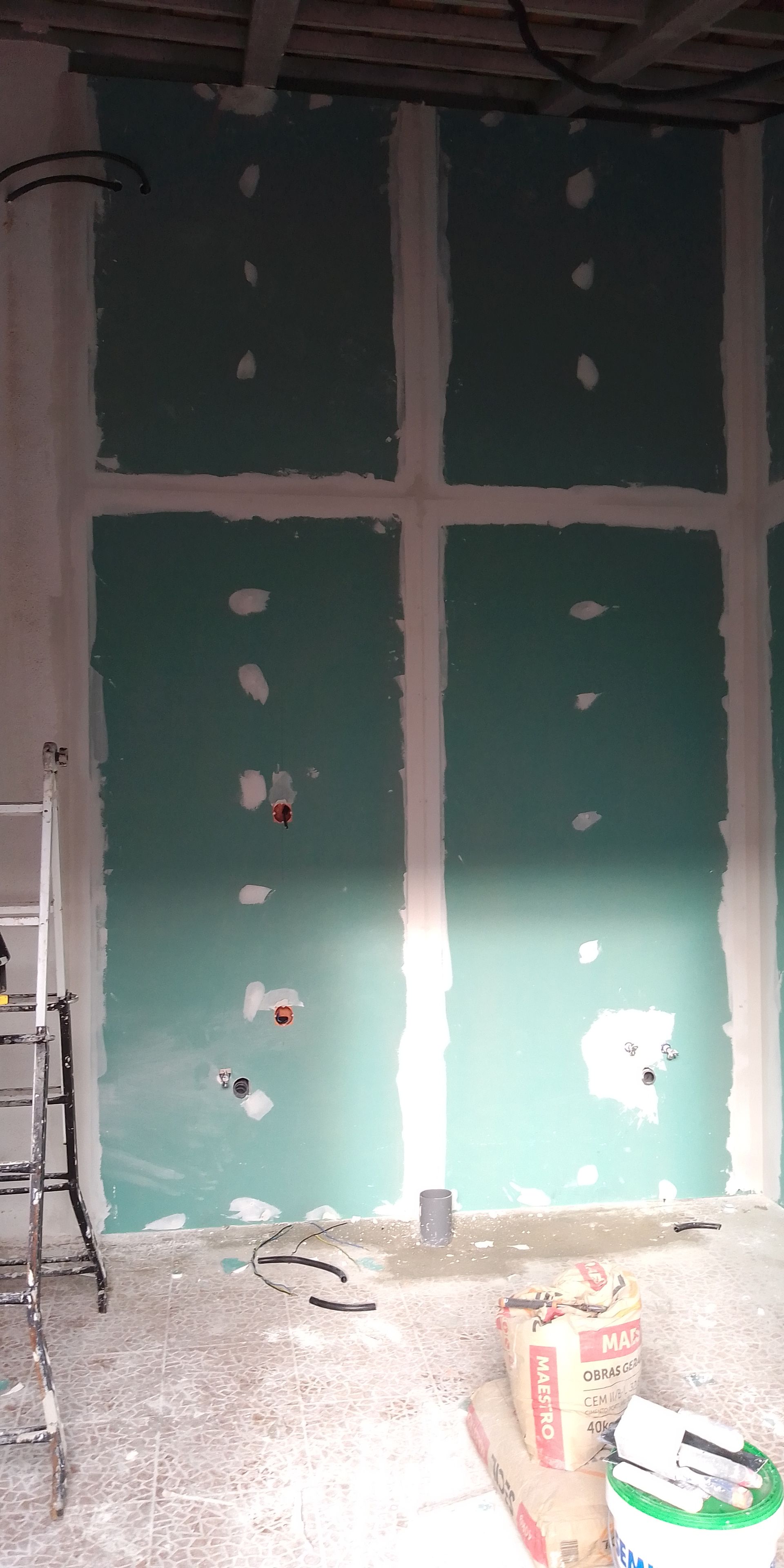 Construção interna com drywall verde instalado, tomadas elétricas visíveis.