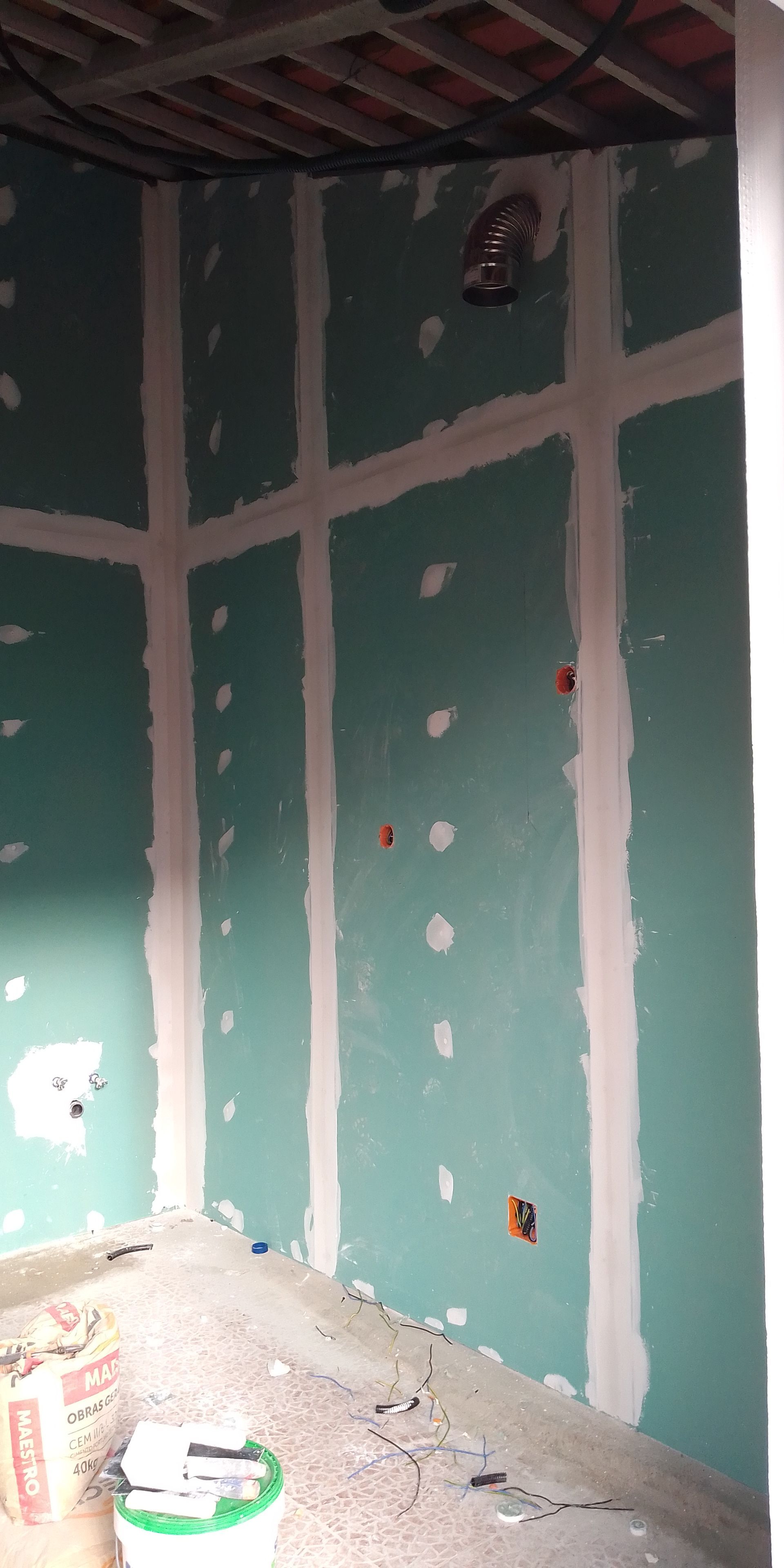 Interior de uma sala em construção com drywall verde e massa corrida branca.