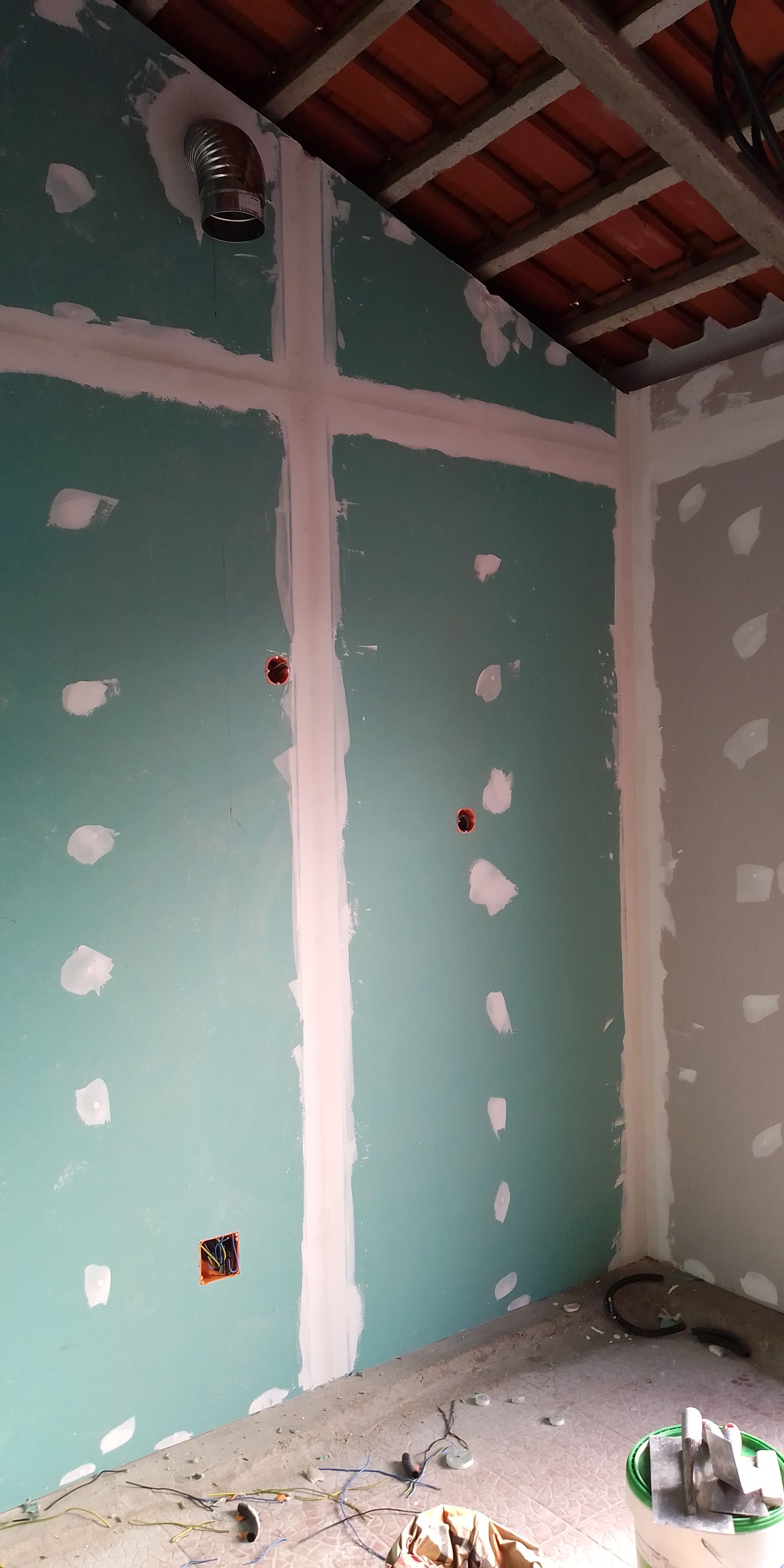 Interior de um cômodo em construção com paredes de gesso acartonado verde, juntas seladas com fita e teto parcialmente aparente.