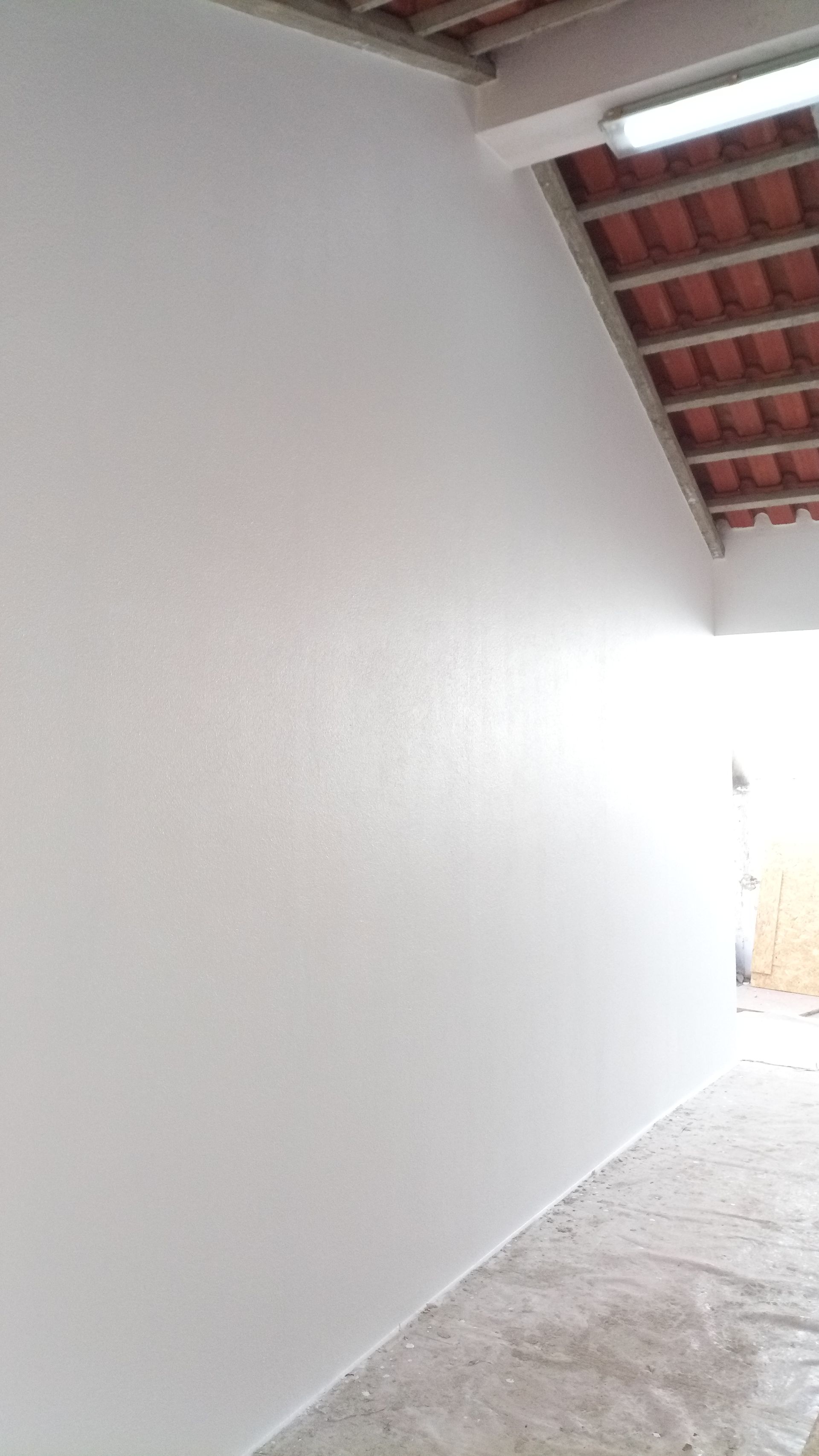 Parede pintada de branco com telhado de telhas acima e piso de concreto abaixo.