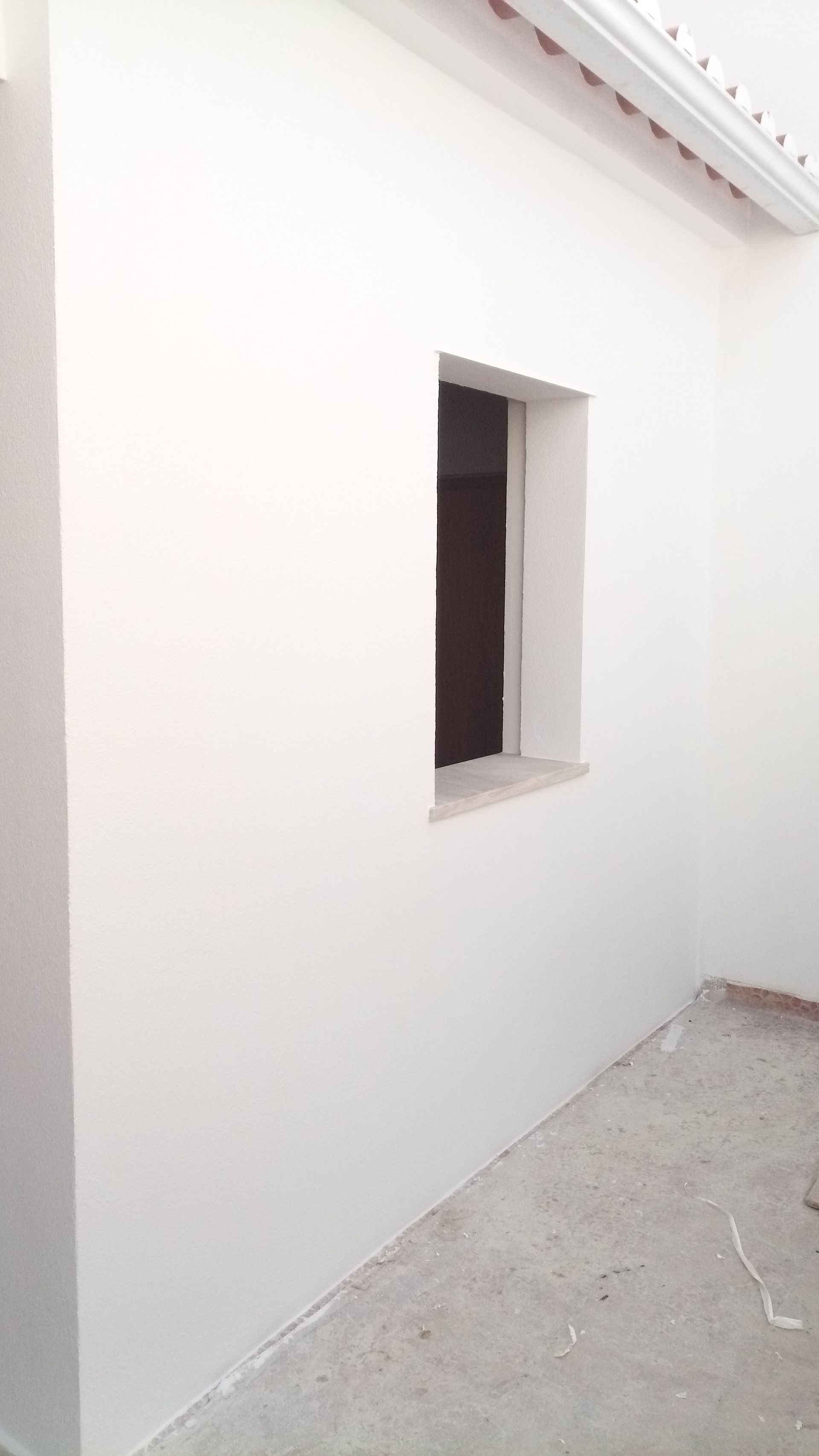 Parede externa branca com uma pequena janela; piso de concreto na frente.