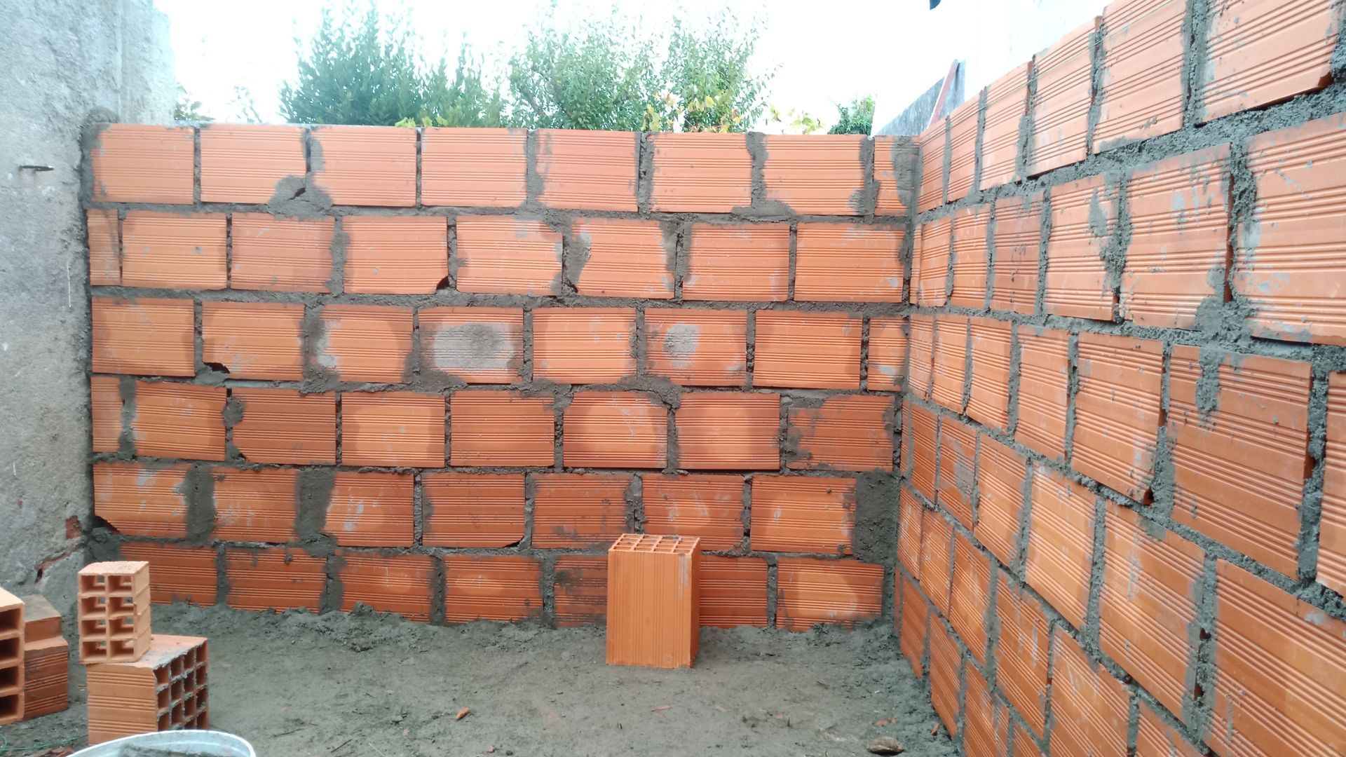 Parede de tijolos em construção, mostrando os tijolos vermelhos assentados com argamassa.